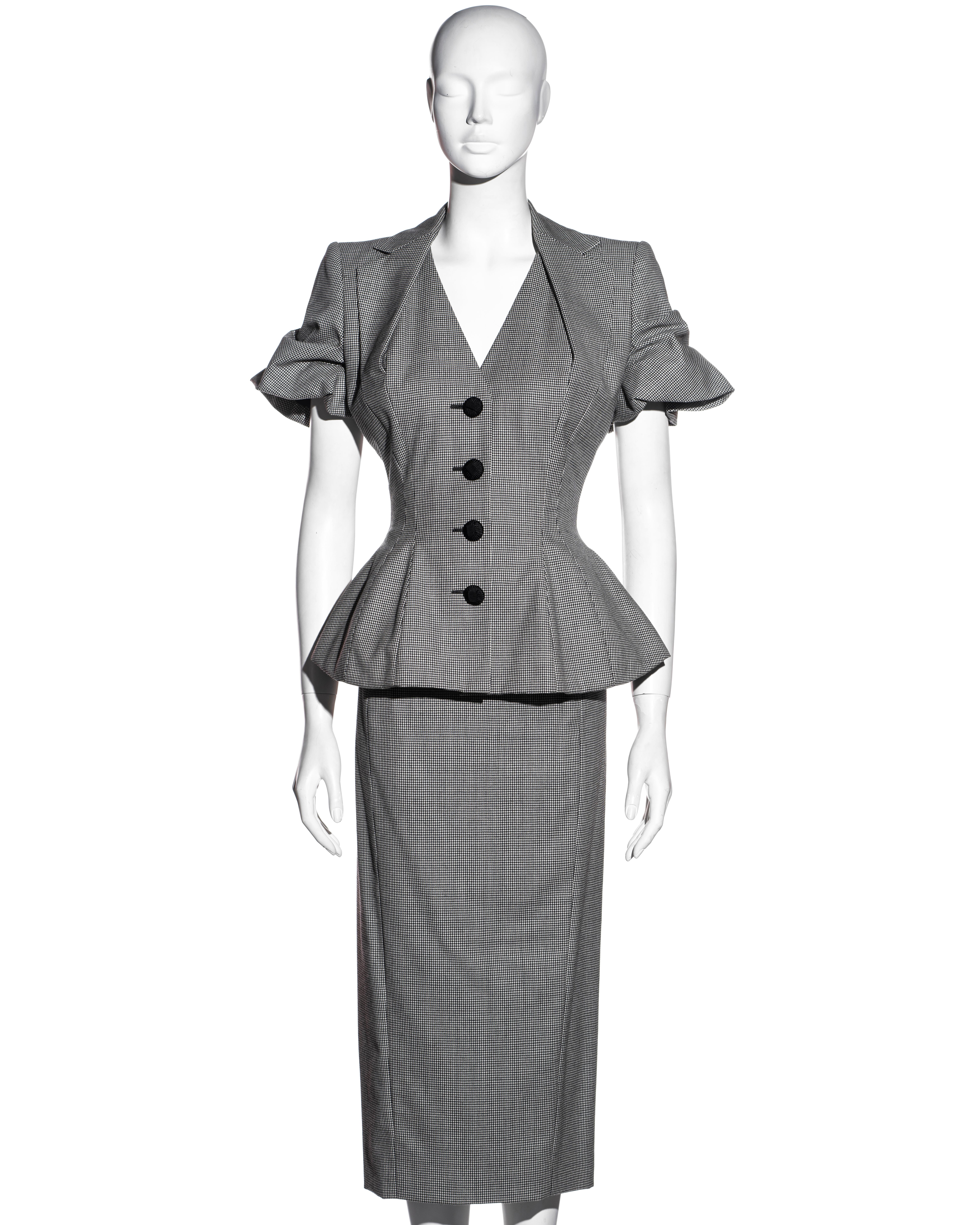 ▪ John Galliano abito con gonna in lana a quadretti pied-de-poule
Giacca a maniche corte
Spalle imbottite
Vita stretta 
Risvolto stile Halter-neck 
Pulsanti rivestiti di corda 
Gonna a tubino sotto il ginocchio abbinata, con piega sul