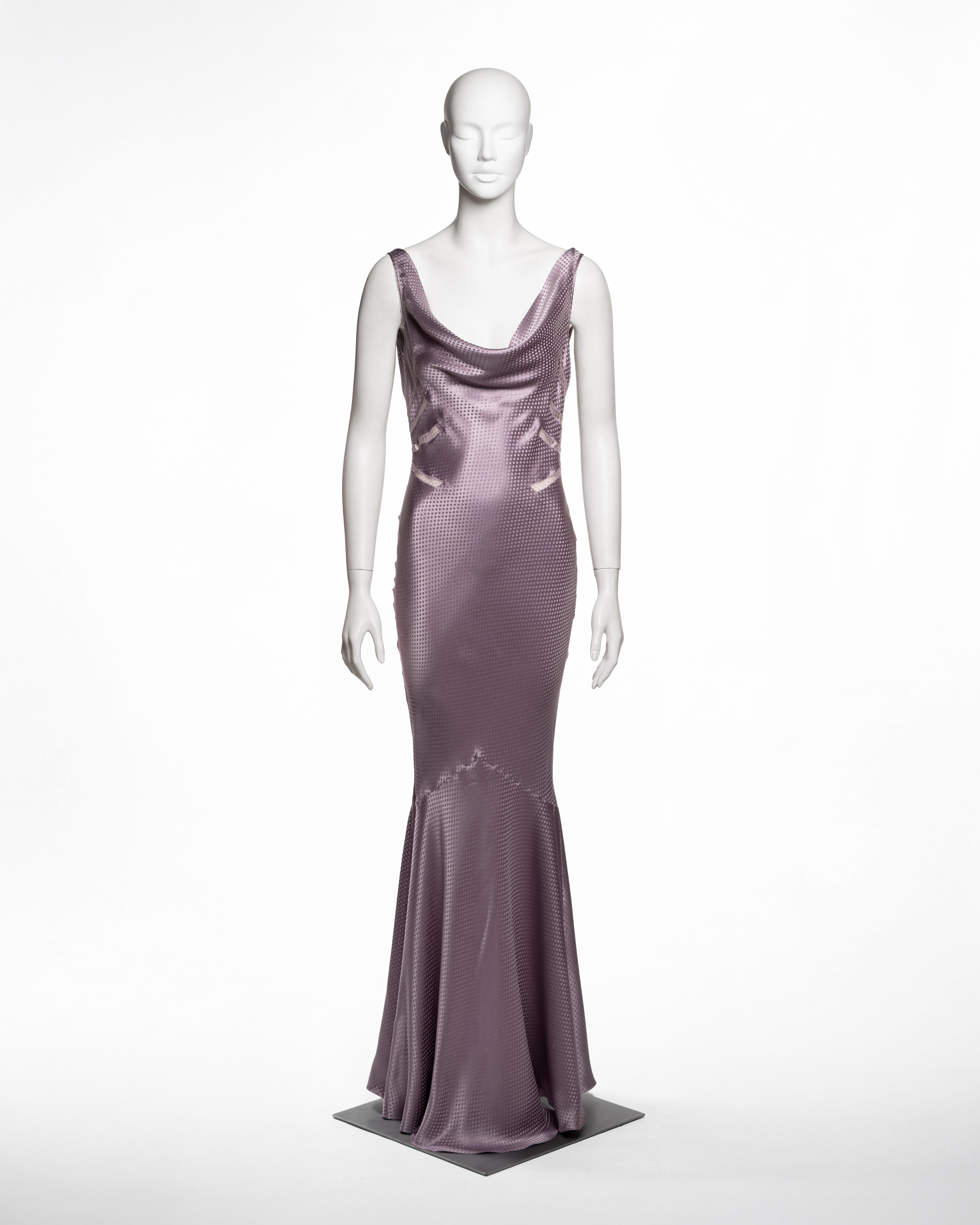 Cette robe longue de la collection automne-hiver 2004 de John Galliano est réalisée en jacquard de satin de soie lavande et présente un motif tissé à pois. La coupe en biais crée une silhouette fluide et ajustée qui s'évase subtilement vers