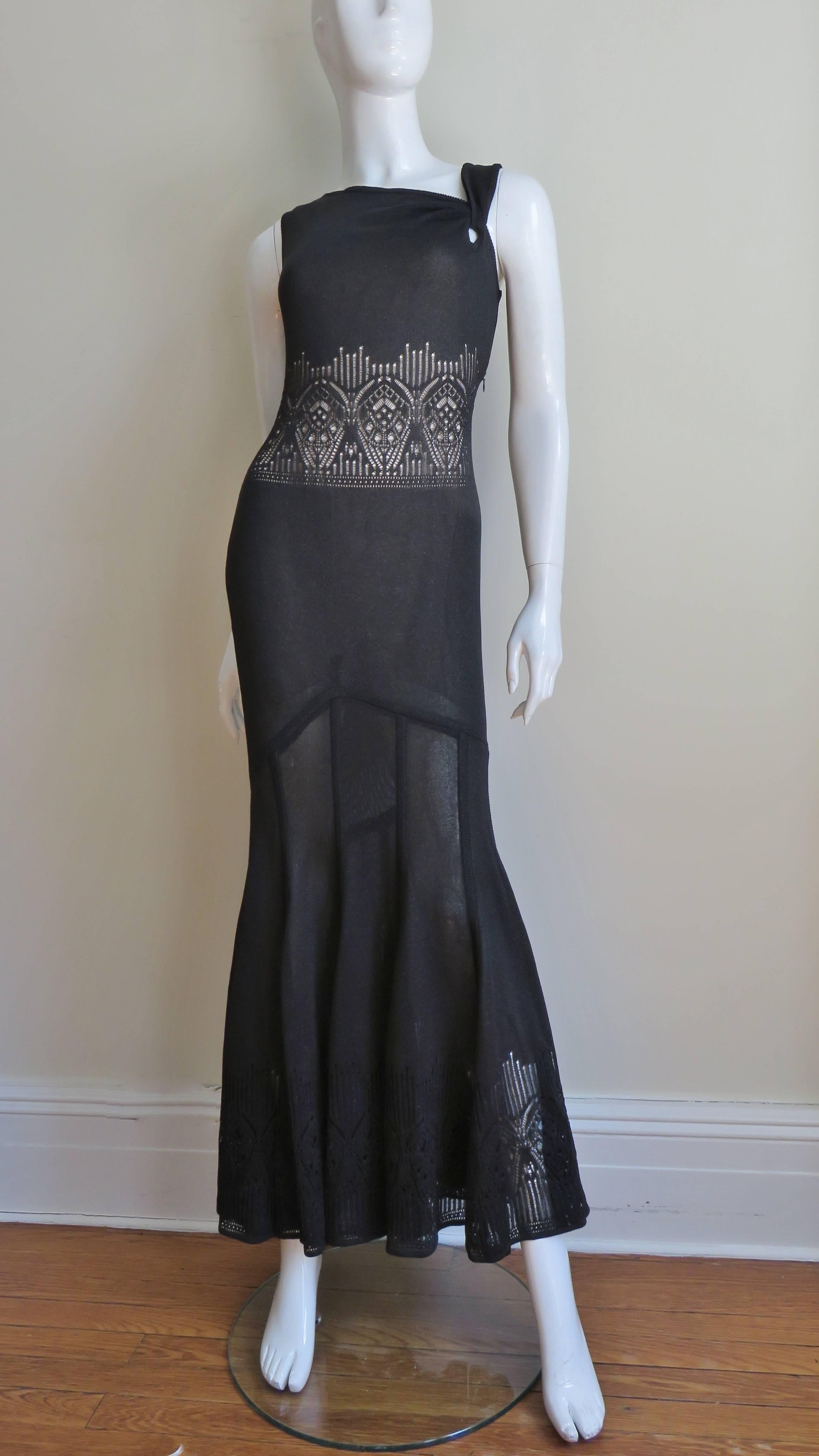 A fabulous black knit dress from John Galliano.  It has an asymmetric angled neckline and semi sheer abstract pattern lace around the midriff and hem. Fitted through the thighs with an inverted V in the center front it has a vertically seamed semi