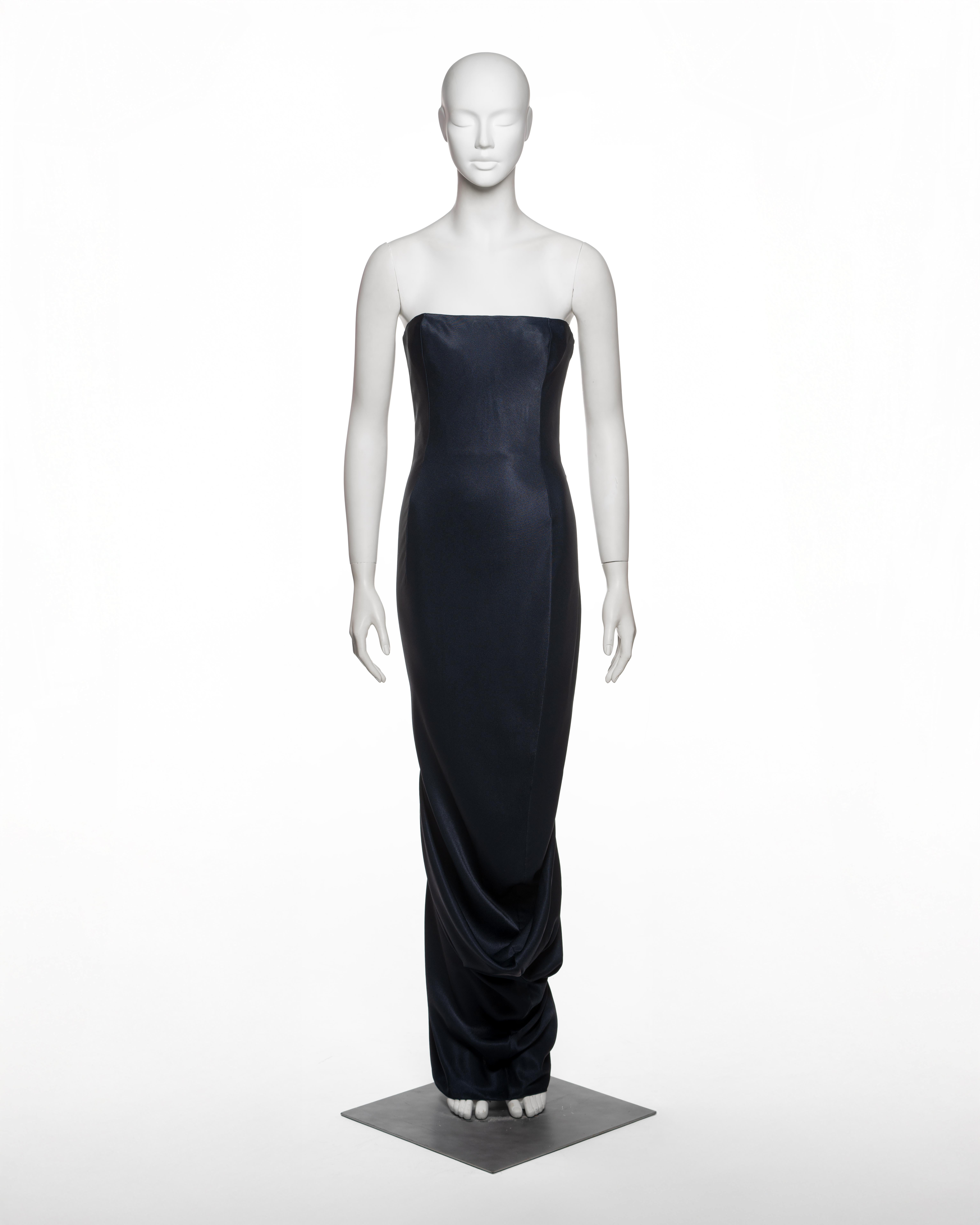 Vestido de noche diseñado por John Galliano para su colección Otoño-Invierno 1995, confeccionado en crepé satinado azul noche. La silueta columnar sin tirantes está moldeada con precisión con un corpiño integrado, reforzado con varillas internas y
