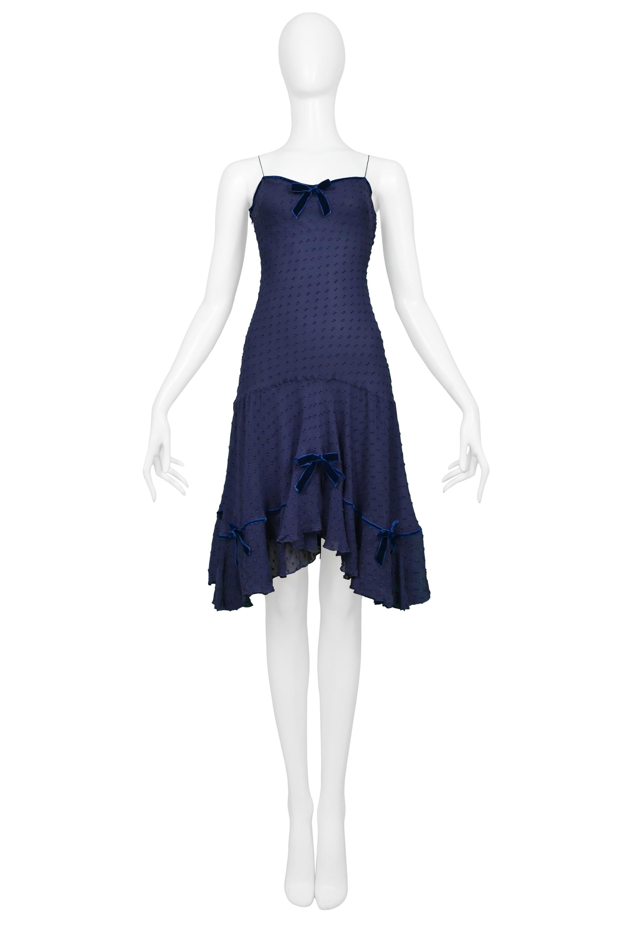 Resurrection Vintage is excited to offer a vintage navy blue John Galliano slip dress featuring classic Swiss dot fabric, blue velvet ribbon bows at the neck and skirt, ruffles along the hemline, side buttons with added zipper, and skinny