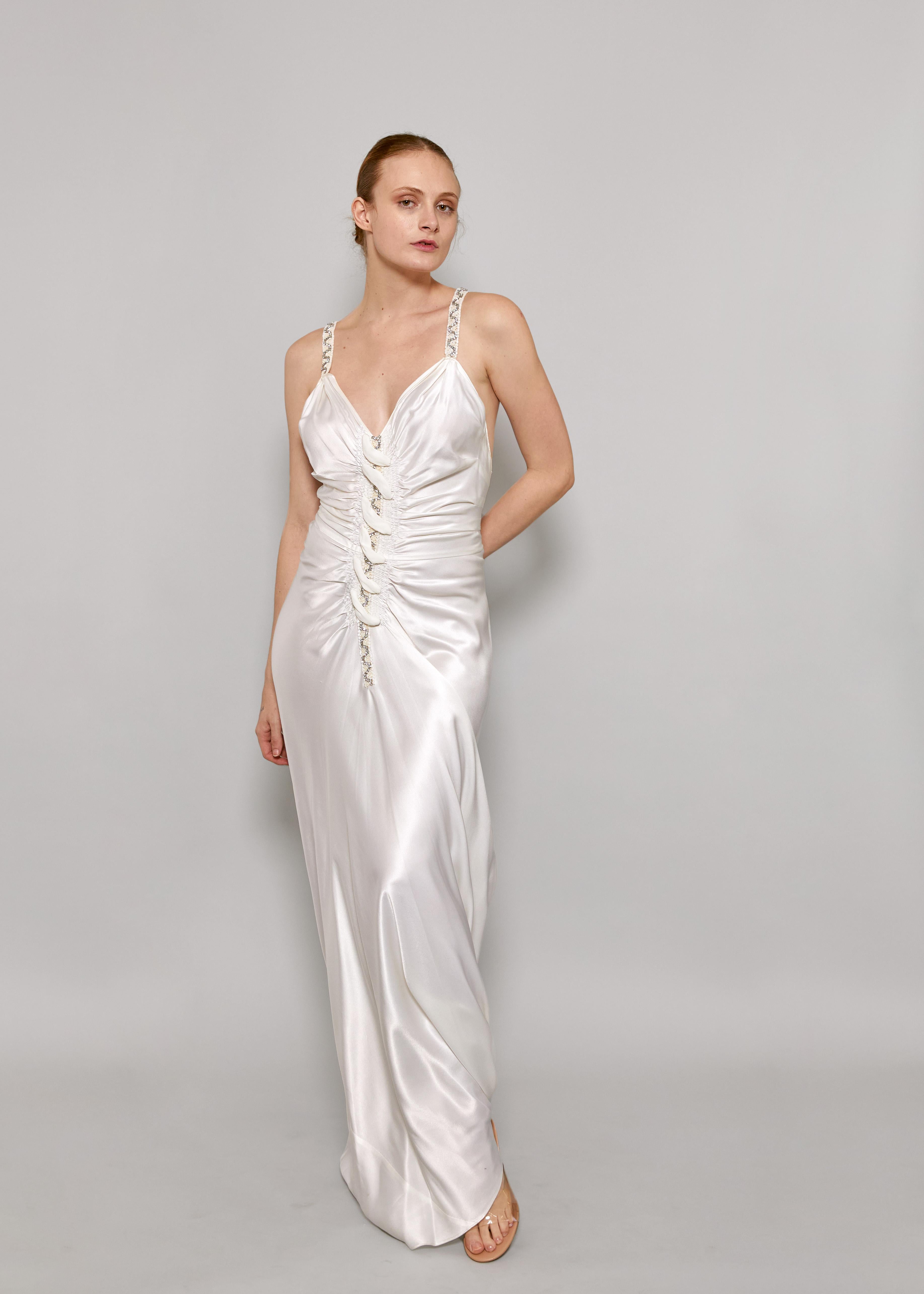 Soyez au centre de l'attention dans l'exquise robe coupée en biais en satin blanc de John Galliano S/S 2006. D'élégantes bretelles ornées de strass et de perles ajoutent une touche de glamour à l'élégant modèle ruché sur le devant. Confectionnée