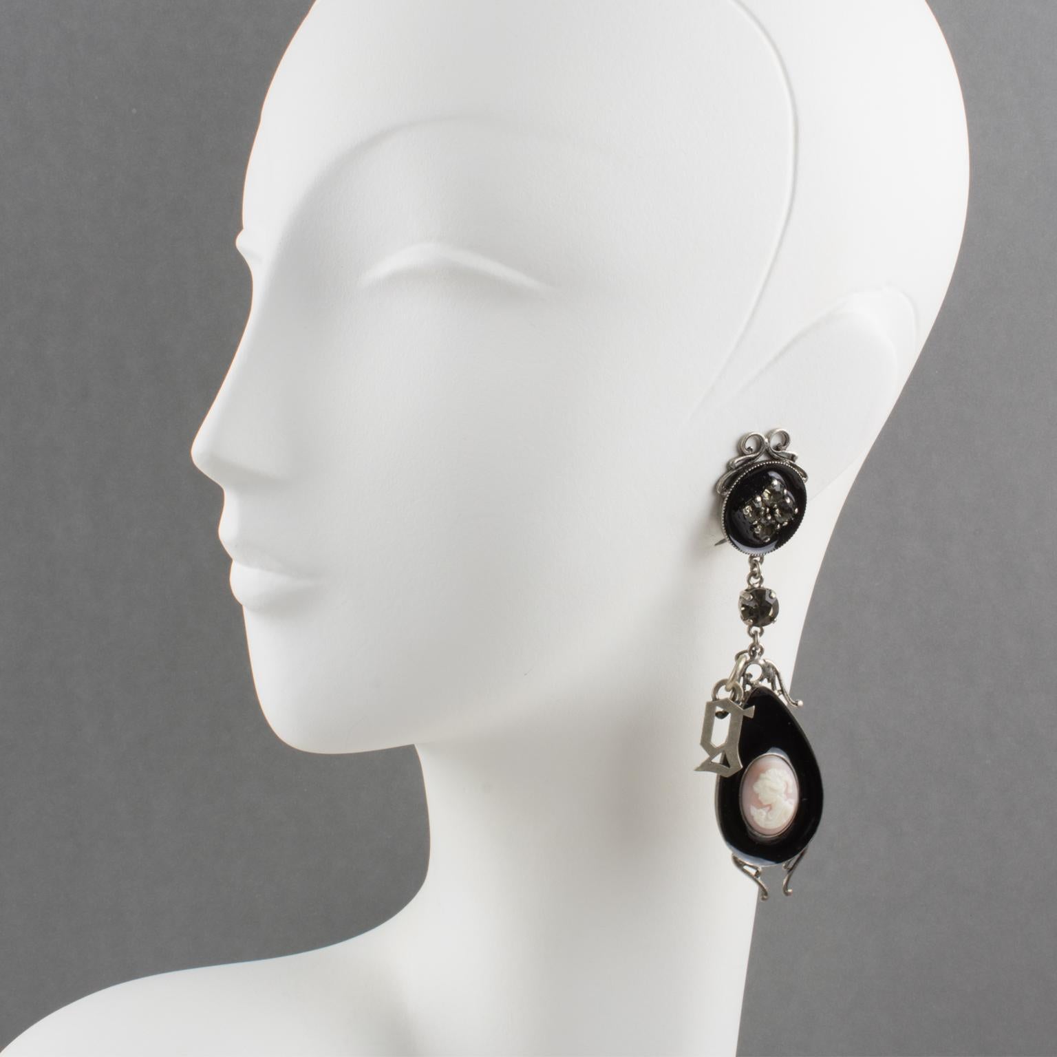 These sophisticated John Galliano Paris clip-on earrings feature a Victorian-inspired design made with silvered metal framing topped with black enamel and resin cameo and complemented with smoked crystal rhinestones. The dangling 