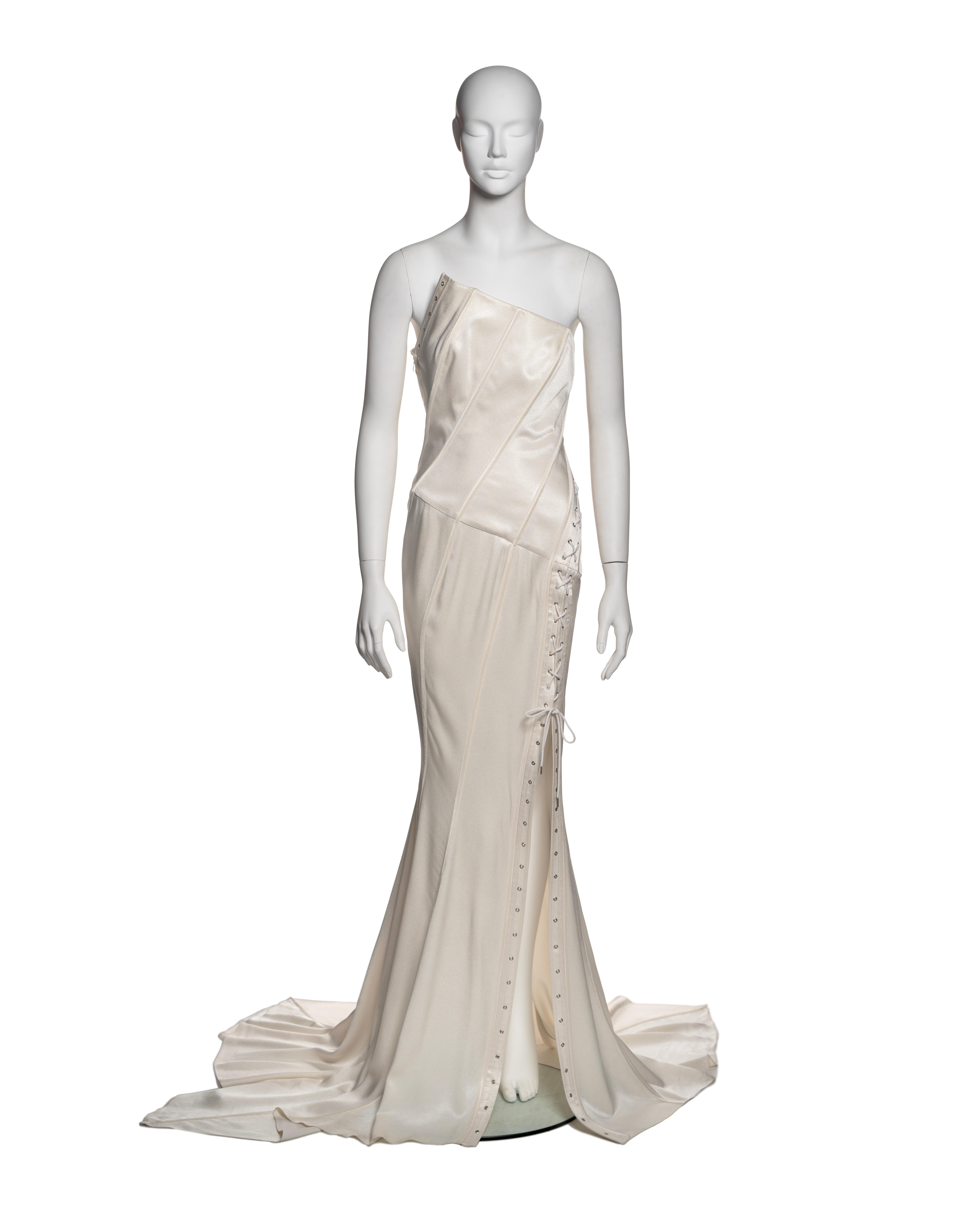 This John Galliano gown from the Spring-Summer 2000 collection is crafted in white bias-cut satin. The design features an asymmetric, strapless neckline with architectural seam detailing and diagonal panel construction. The gown incorporates