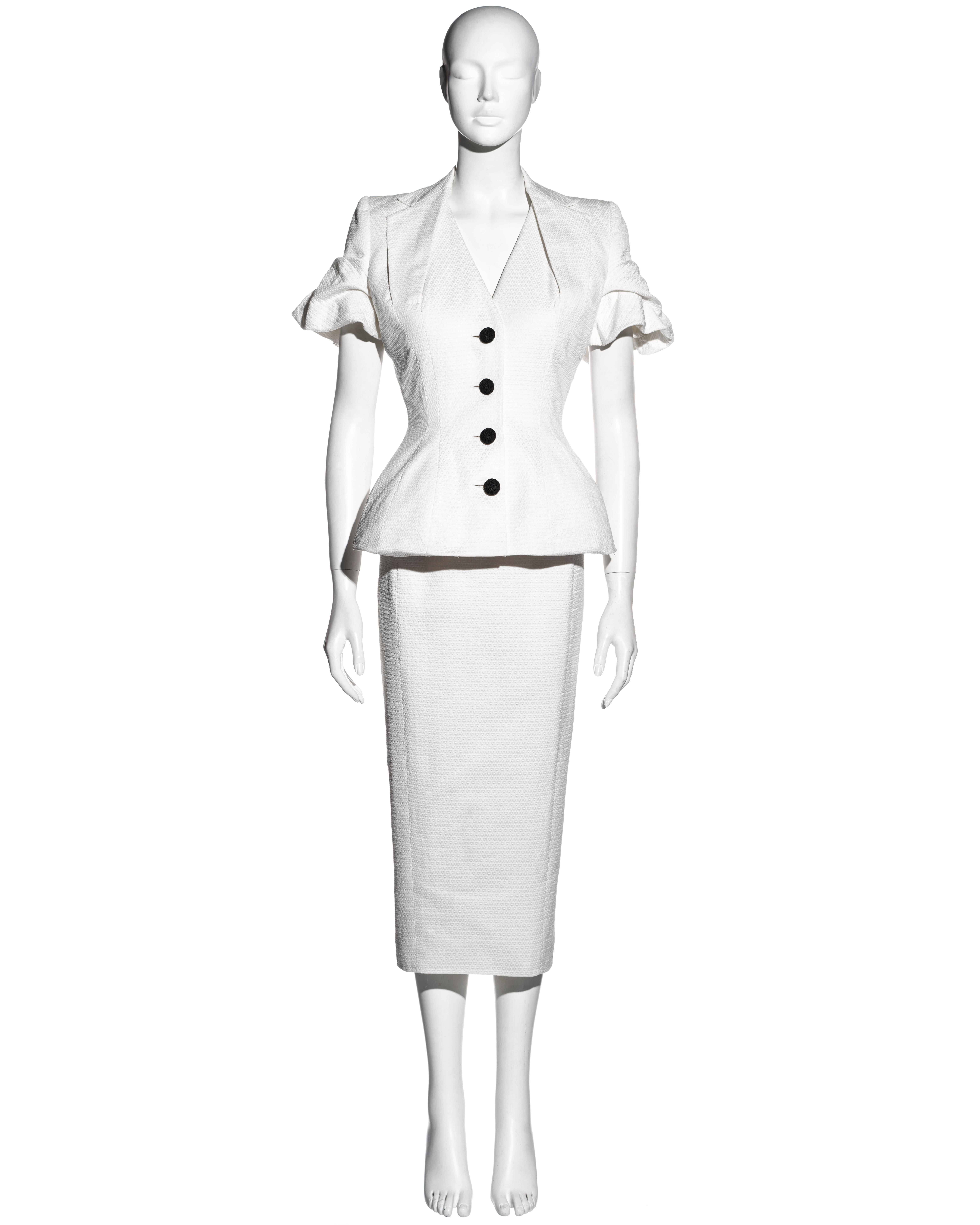 ▪ John Galliano white pique cotton jacket and dress showpiece ensemble 
▪ Short-sleeved jacket 
▪ Padded hips and shoulders 
▪ Nipped waist  
▪ Halter-neck style lapel  
▪ Black cord-covered buttons  
▪ Matching sheath dress with kick-out vent at