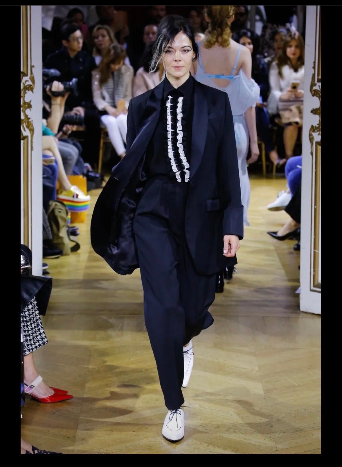 John Galliano blazer with a masculine allure , from the fall 2018 catwalk.
Long and straight with a tuxedo shawl collar , closes with a single button.
2 flap pockets and pretty buttoned lapel cuffs.
Slit back.
In black virgin wool with acetate and