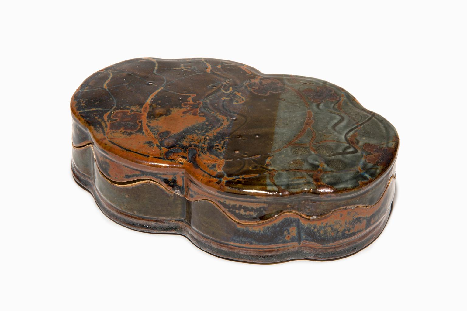 "Scalloped Box" is a stoneware piece with the decorative layer of the rich earth toned glazes and markings that John was so well-known for. He was, also, known for the undulating lip lines that fit together like a puzzle on his exquisite boxes. This