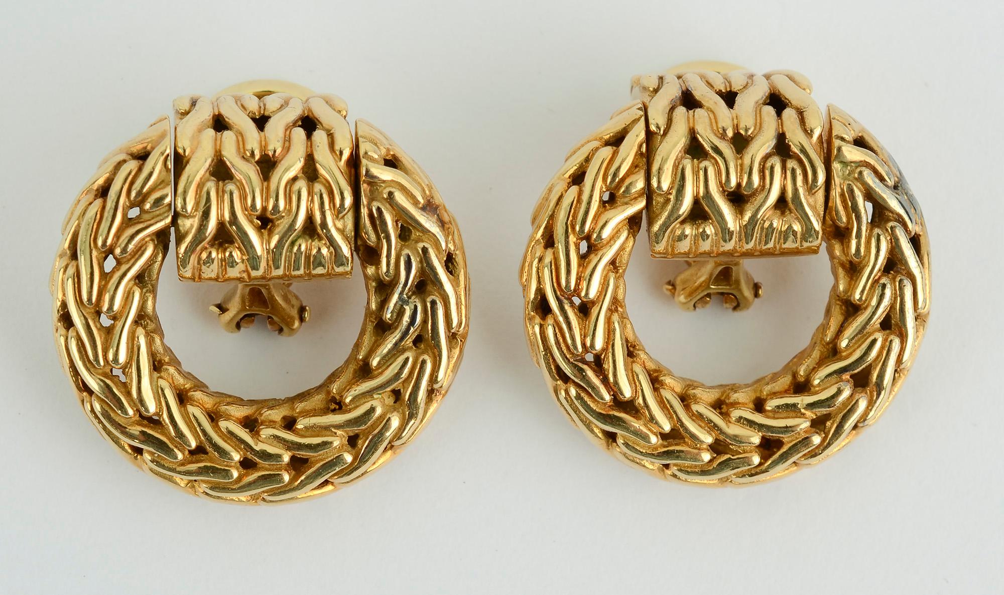 John Hardy 18 karat gold earrings in the woven design he so often favors. At the top of the circle is a movable curved band giving the earrings some play when worn. Clip backs can be converted to posts. The earrings are 1 inch in length and 15/16