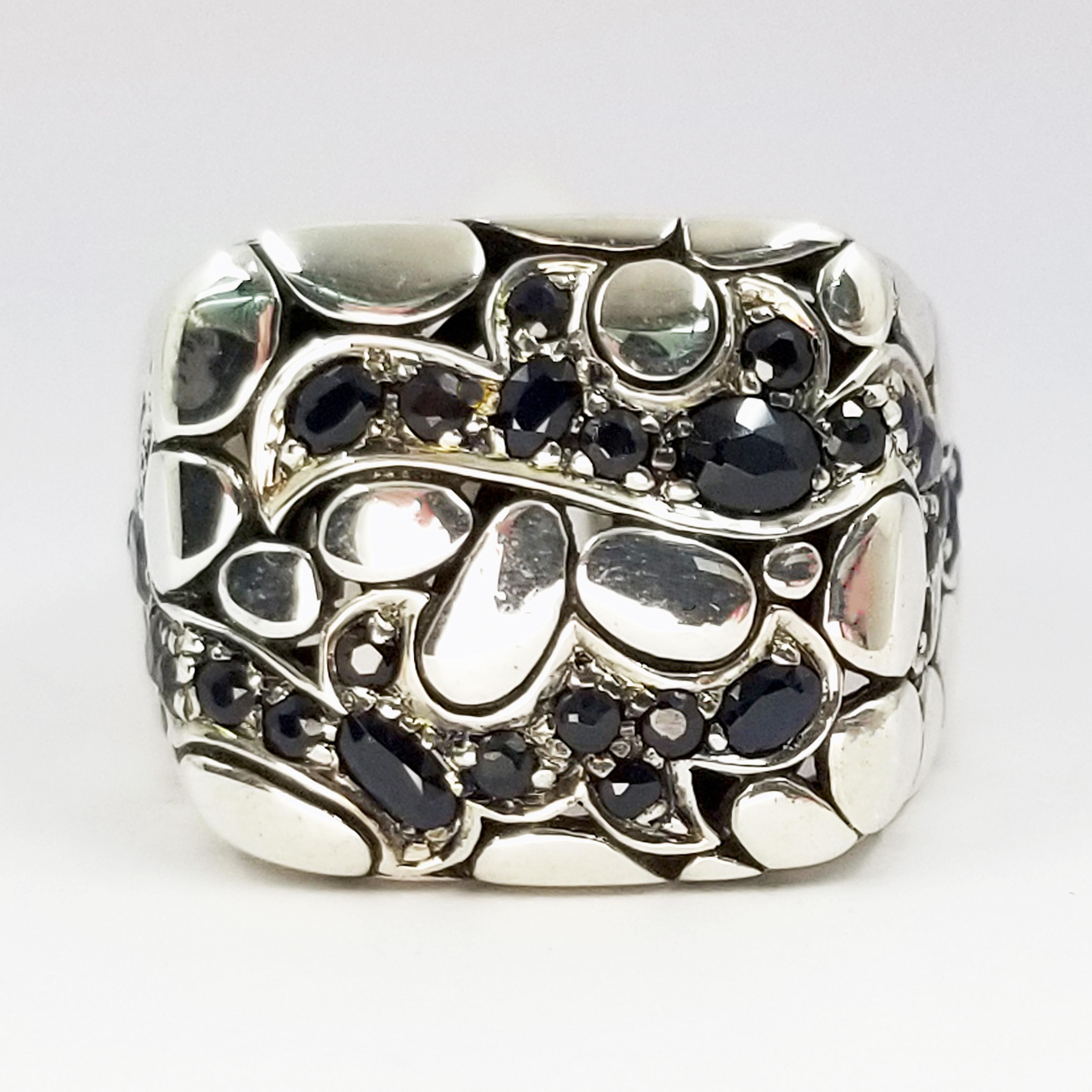 This sterling silver ring is hand assembled in Bali by the craftsmen at John Hardy. It is from the men's Dayak jewelry collection, and features multiple prong-set faceted black sapphires on the top and sides. The interior gallery is designed with a