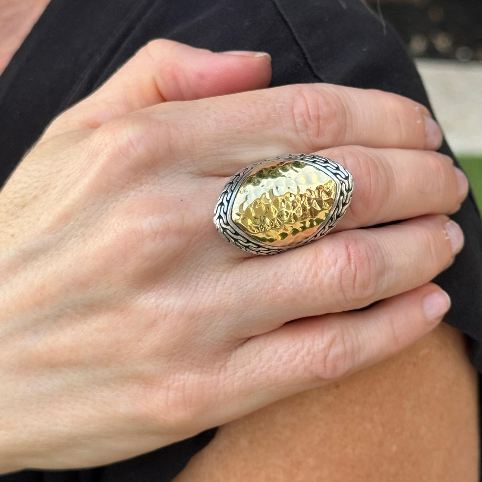 This Sterling Silver and 18K Yellow Gold John Hardy Palu Hammered Saddle Ring is a bold and sculptural statement piece, featuring a beautifully contoured saddle shape with a top measuring approximately 20 x 35mm. The ring showcases John Hardy’s