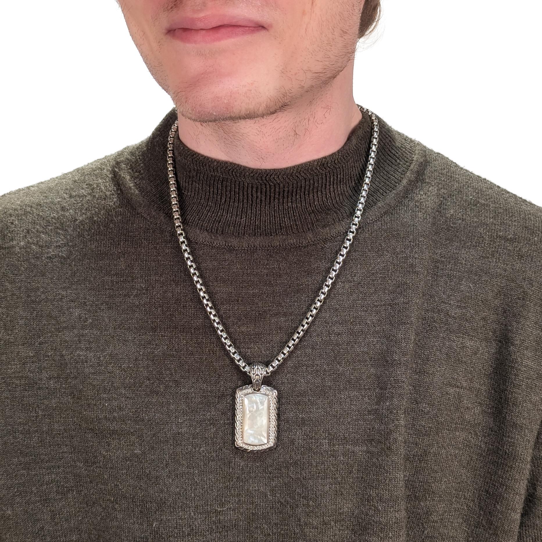 By John Hardy.

In sterling silver.

Bezel-set with a large, faceted mother-of-pearl cabochon surrounded by a halo of round white sapphires. 

The pendant engraved to the reverse with a serpent (Naga) coiled around a sword and with a cable pattern