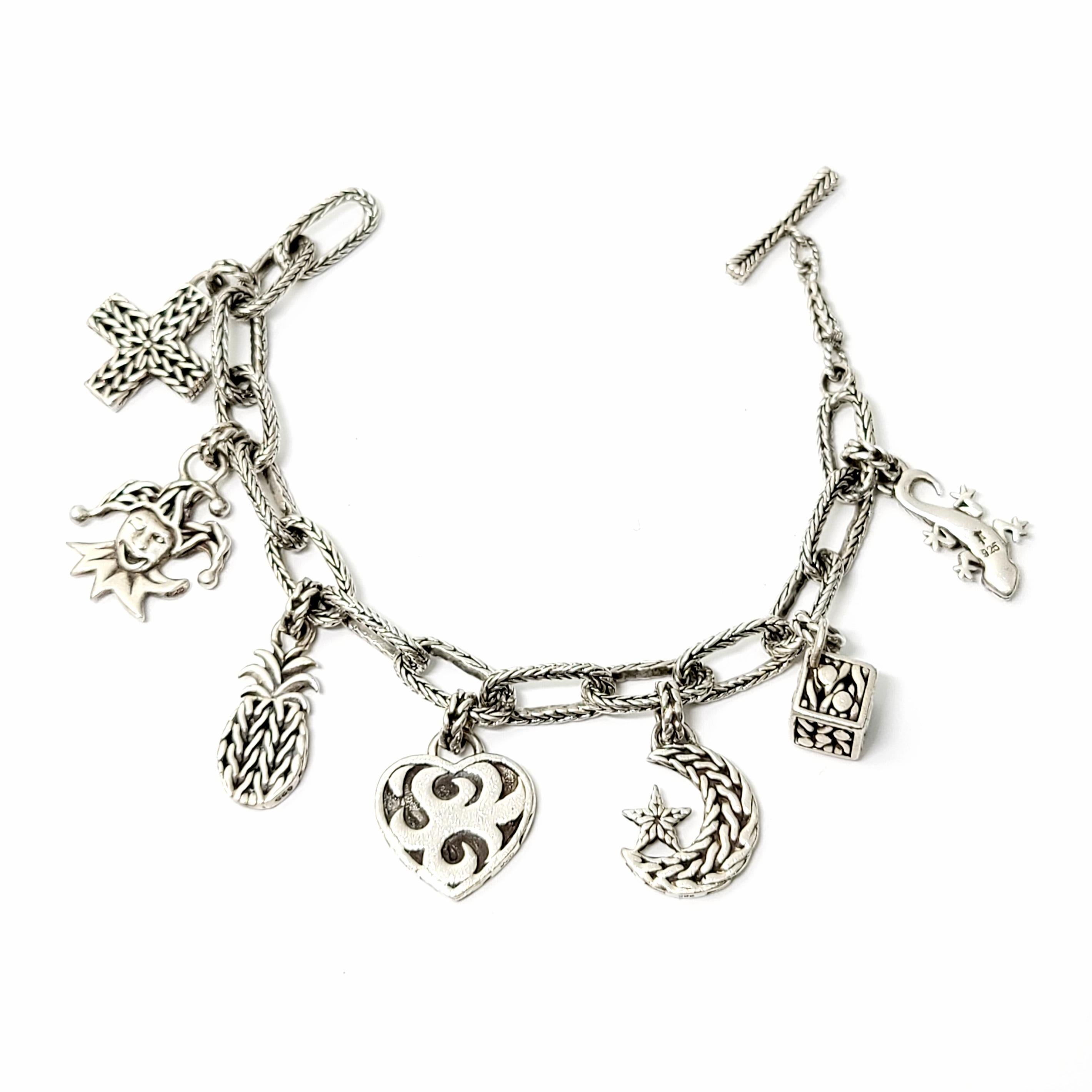 John Hardy sterling silver charm bracelet with 7 charms.

This oval link charm bracelet includes 7 charms: cross, joker, pineapple, heart, moon/star, cube and lizard. Toggle closure on bracelet. Wheat design on the links of the bracelet, as well as