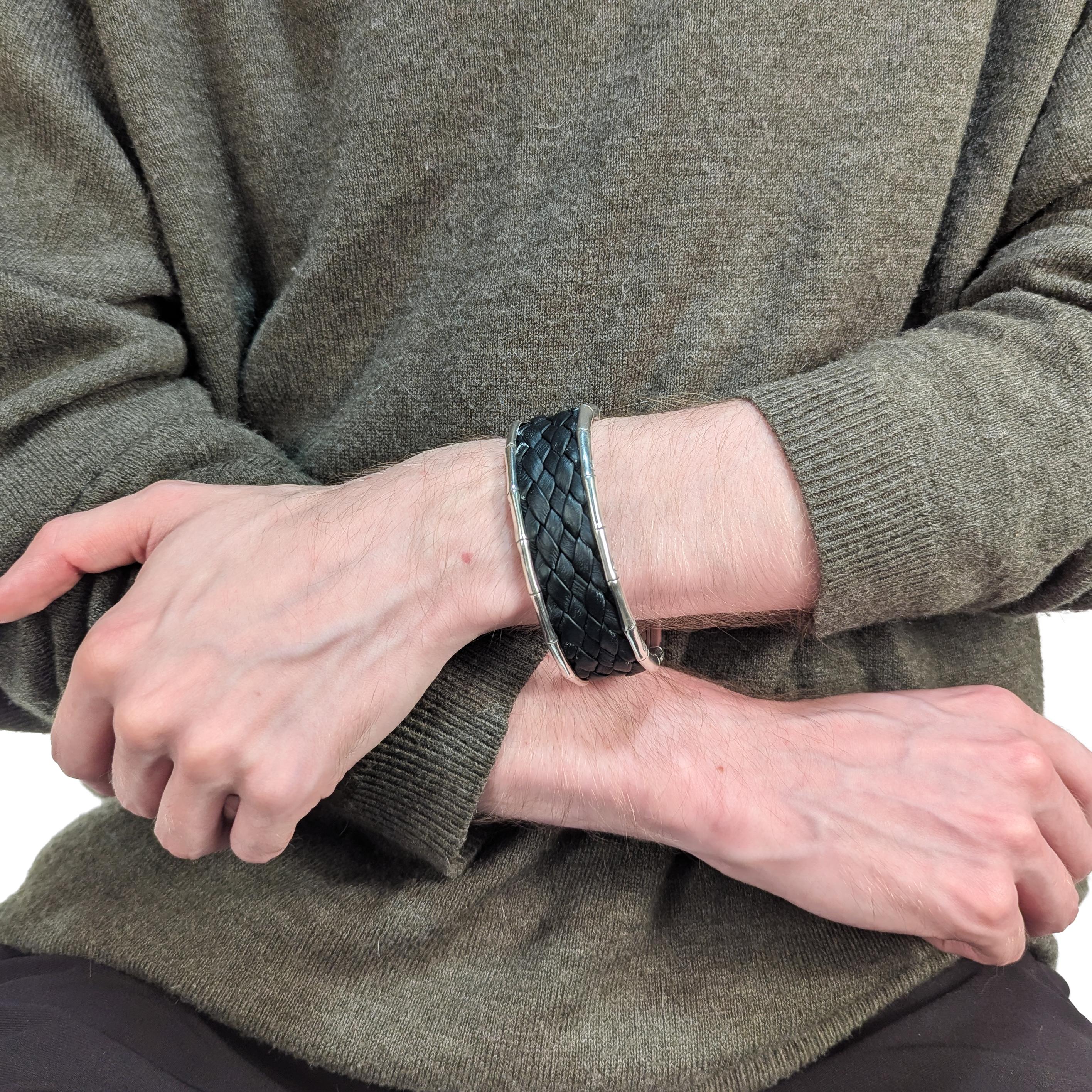 Un bracelet manchette en argent finement signé.

Par John Hardy.

En argent sterling.

Avec couverture en cuir noir matelassé et garniture en bambou stylisé sur les bords de la manchette. 

L'intérieur est gravé d'une représentation d'un artisan