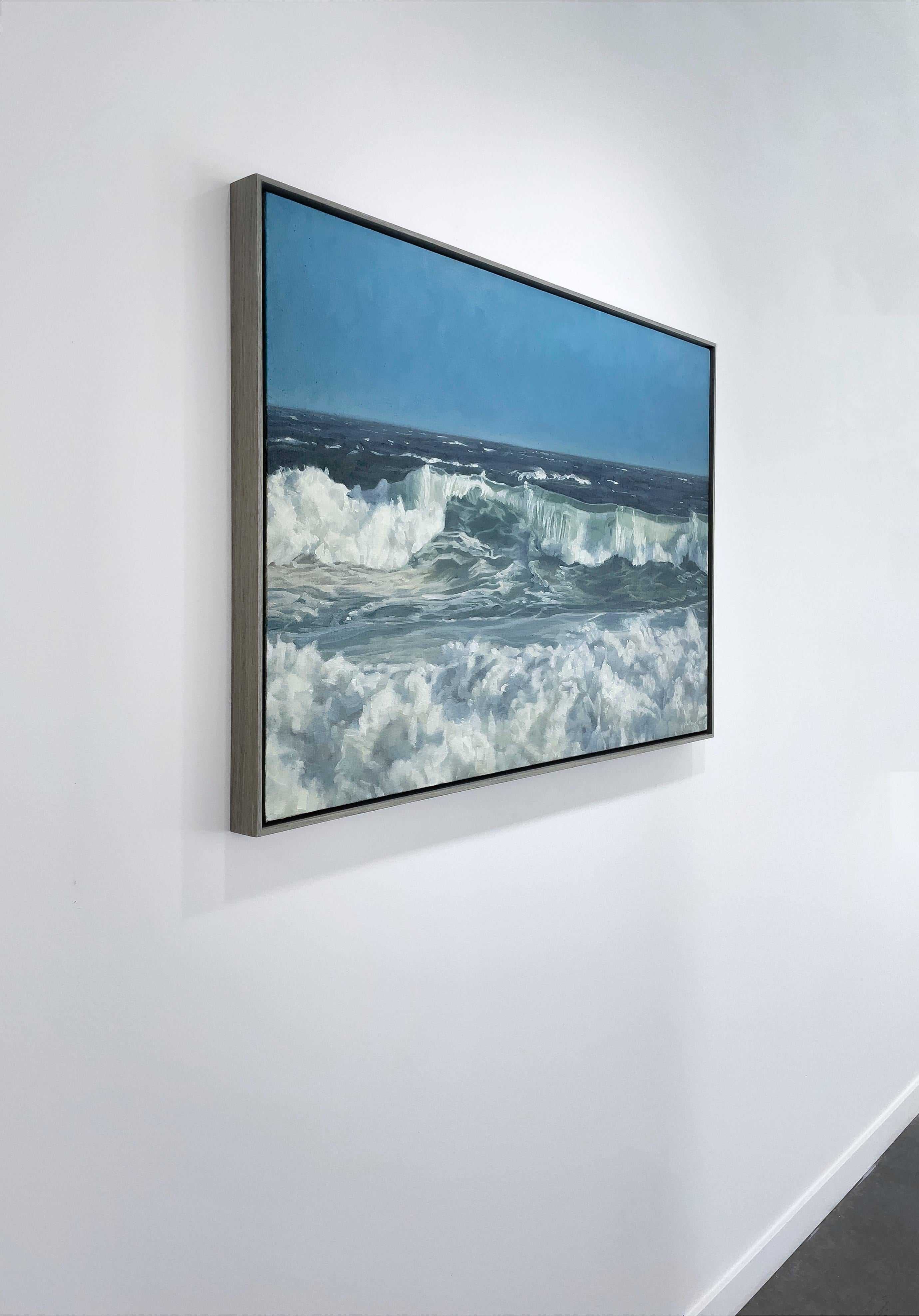Cette peinture à l'huile côtière originale sur lin de John Harris présente une vue très détaillée des vagues de l'océan qui s'écrasent près d'un rivage sous un ciel bleu clair. La pièce présente un mélange de tons bleus froids et de vert de mer, mis