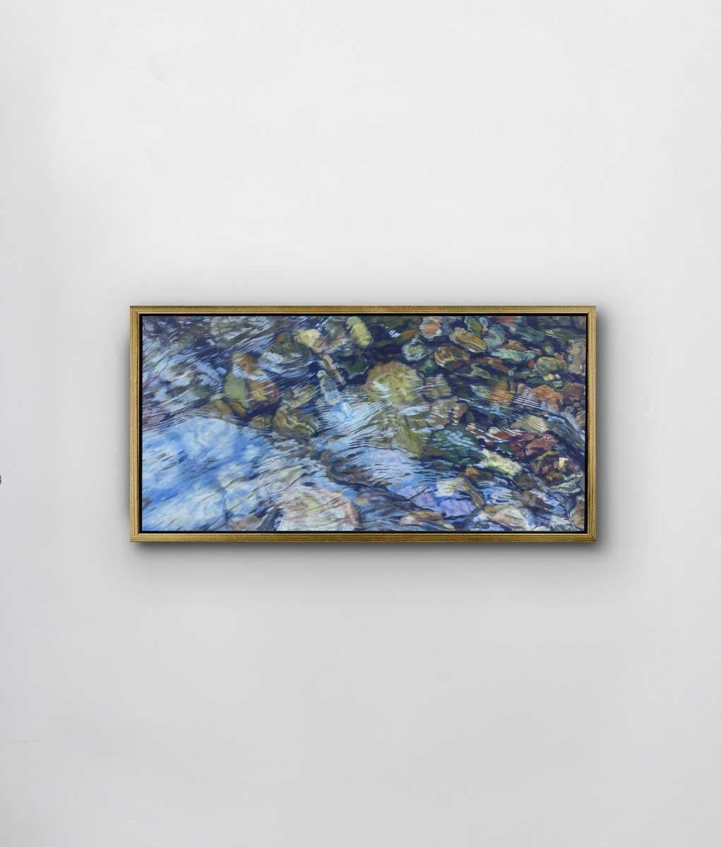 This realistic limited edition print captures a highly detailed view of water flowing over rocks in a river bed. The earth-toned rocks sit under water that is rippling lightly and reflecting light and light shapes from above. Filled with abstract