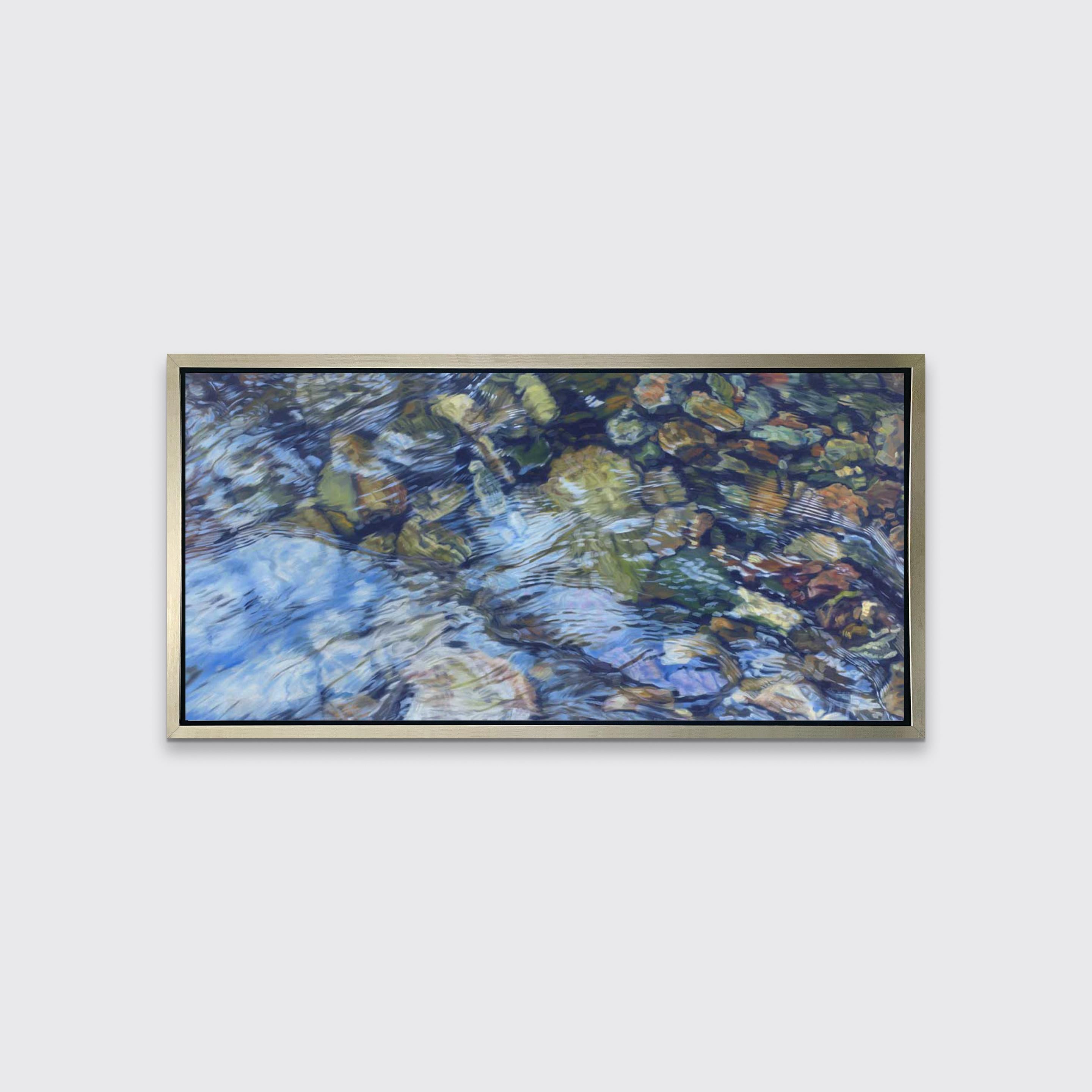 This realistic limited edition print captures highly detailed, close up view of river water running over small, colorful rocks. Above the shapes, textures, and earthy colors of the rocks, the water reflects the light above it. Filled with abstract