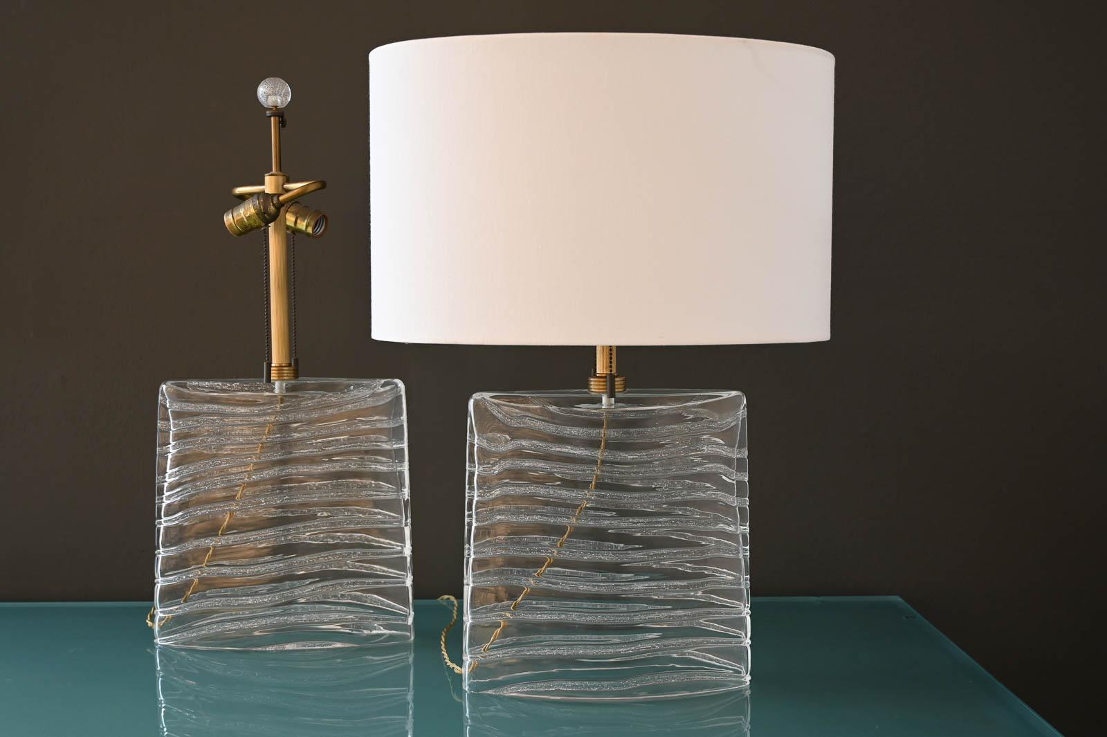 John Hutton for Donghia Murano Glass Lamps in Clear Glass and Brass.  Signed on the base, these beautiful lamps emit soft light and perfect for nightstands or credenza.  Oval shades are NOT included, however we can order new ones for them, please