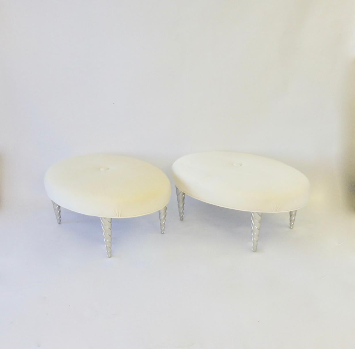 Elegant and sensual oval ottomans designed by John Hutton. Brought in by Angelo Donghia Hutton was director of design 1978 - 1998. This pair covered in cream and white ultra suede are in excellent original condition.