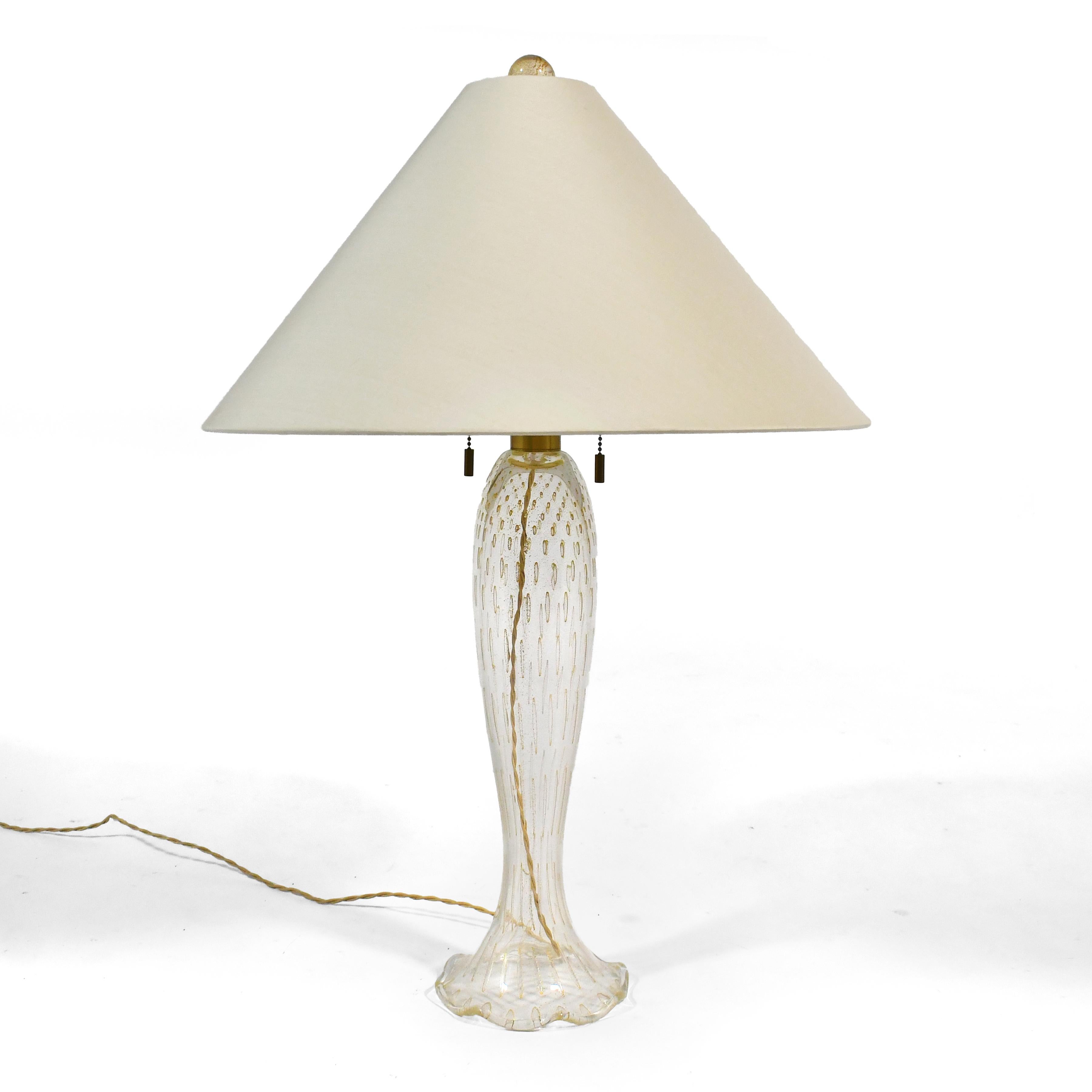 Cette lampe rare et remarquable, conçue par John Hutton pour Dongia, a été fabriquée en verre de Murano Seguso selon la technique du Cordonato D'Oro. Le verre transparent est décoré de bulles capturées, de poussière d'or et d'aventurine d'or. Elle