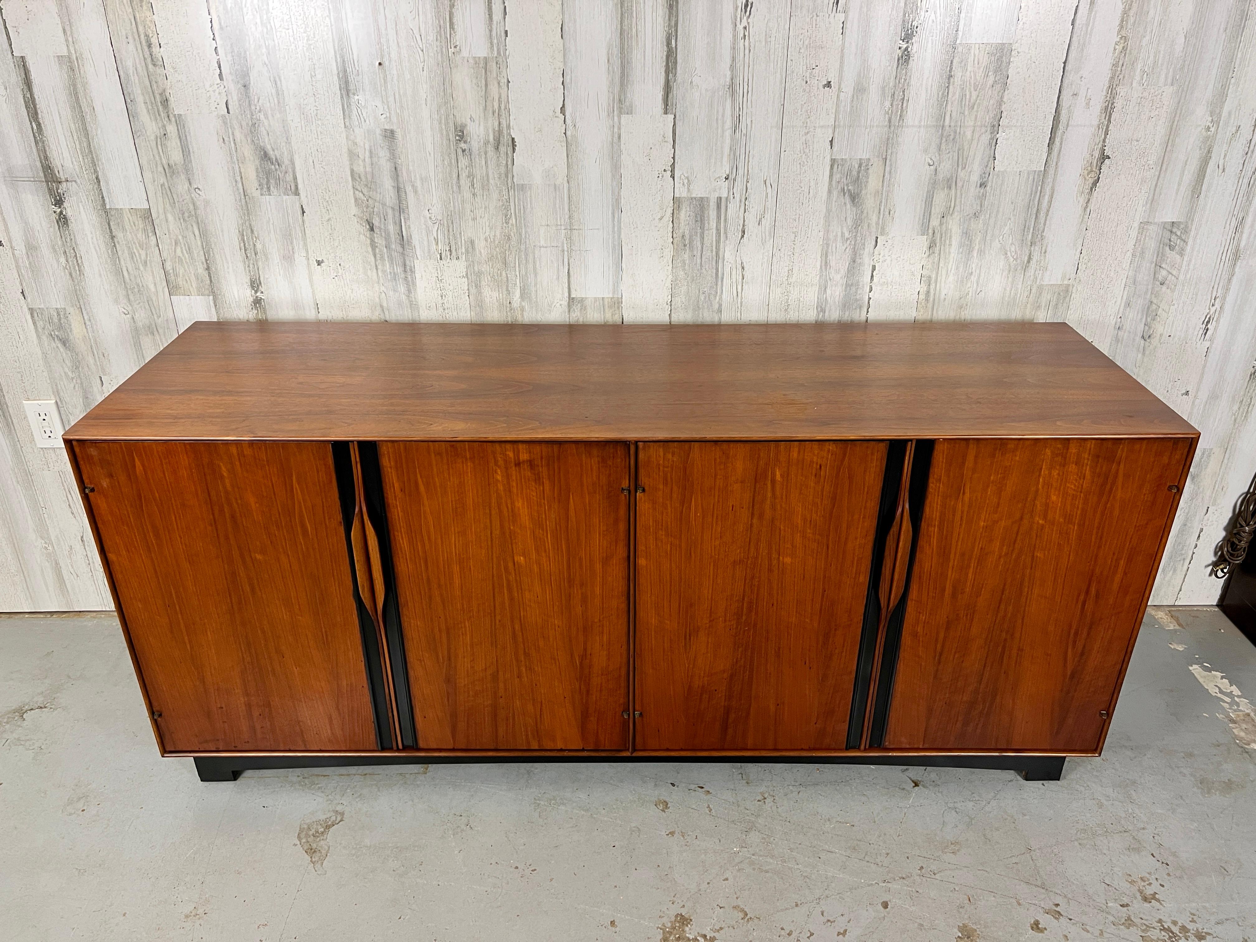 Four door credenza with sculpted walnut handles that open to shelves and drawers.
Beautiful black accents on the doors and base make the walnut pop.
Designed by John Kapel for Glenn of California furniture.