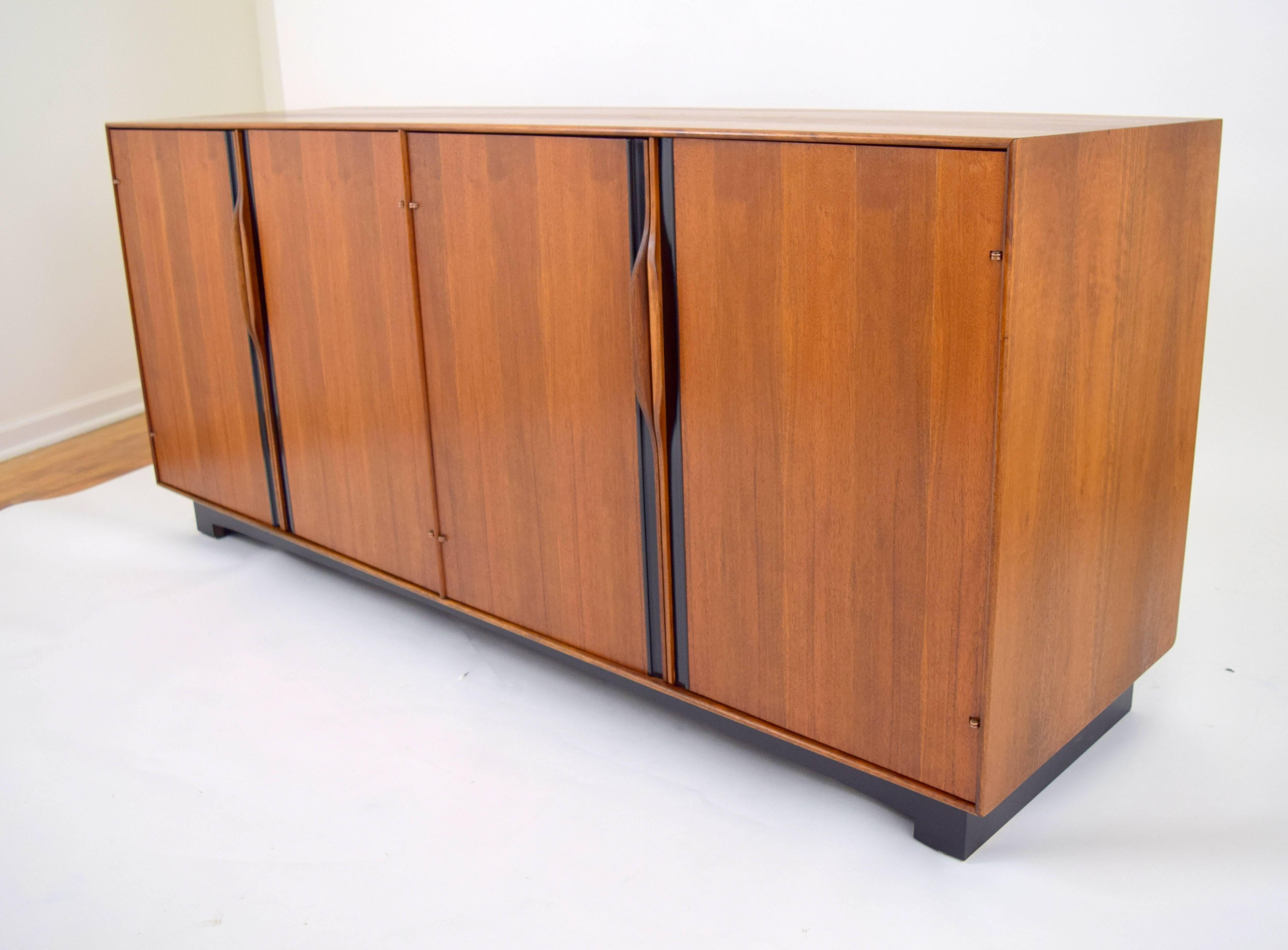 John Kapel for Glenn of California walnut credenza or sideboard with sculpted walnut handles and black plastic inlay. Four doors conceal one adjustable interior shelf on each side, and two shallow drawers on one side. Lovely oiled walnut case with