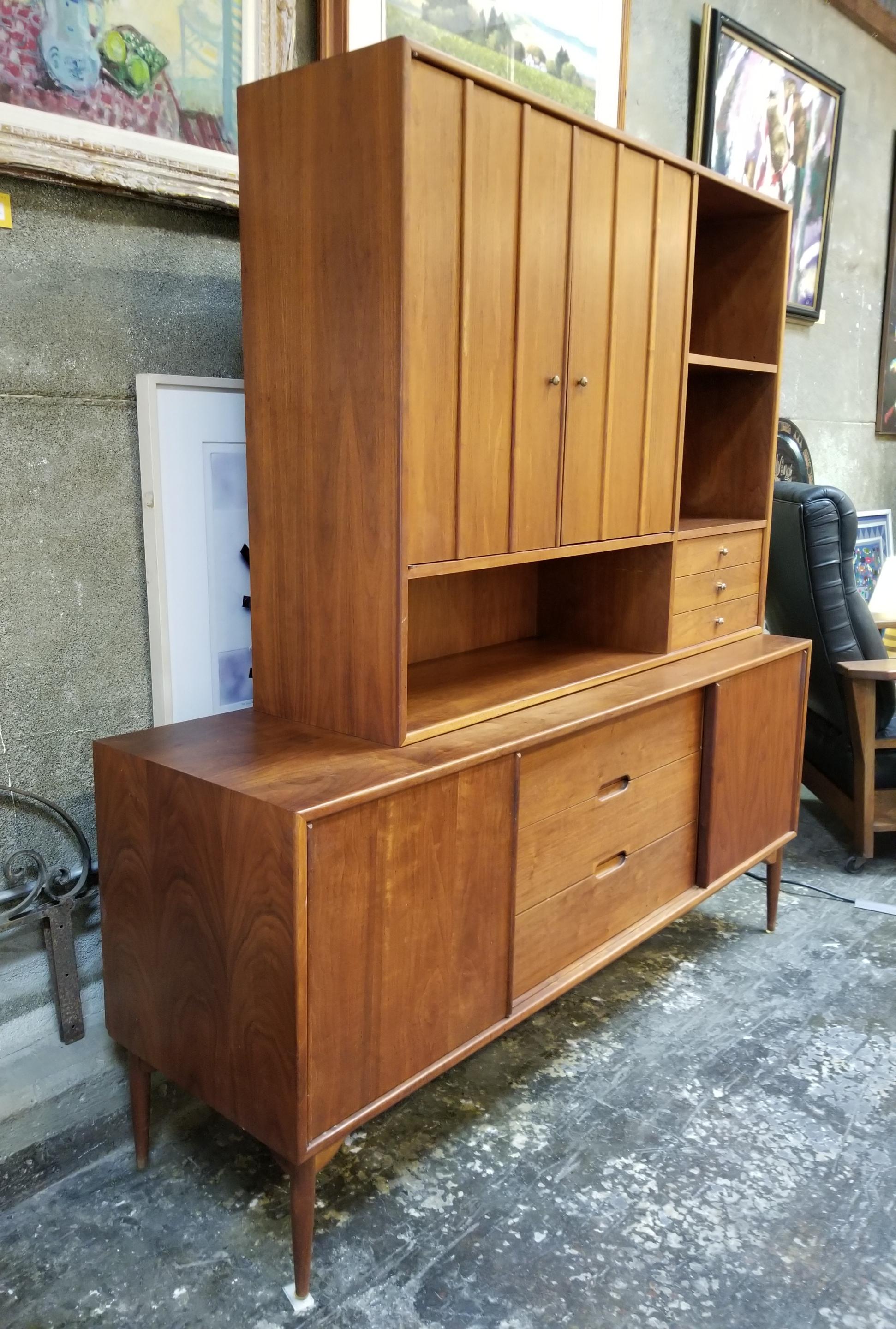 A two piece storage cabinet designed by John Keal for Brown-Saltman of California. Features two sliding doors opening to storage with adjustable shelf interior and three center drawers. Upper unit consists of three small drawers, open shelving and a