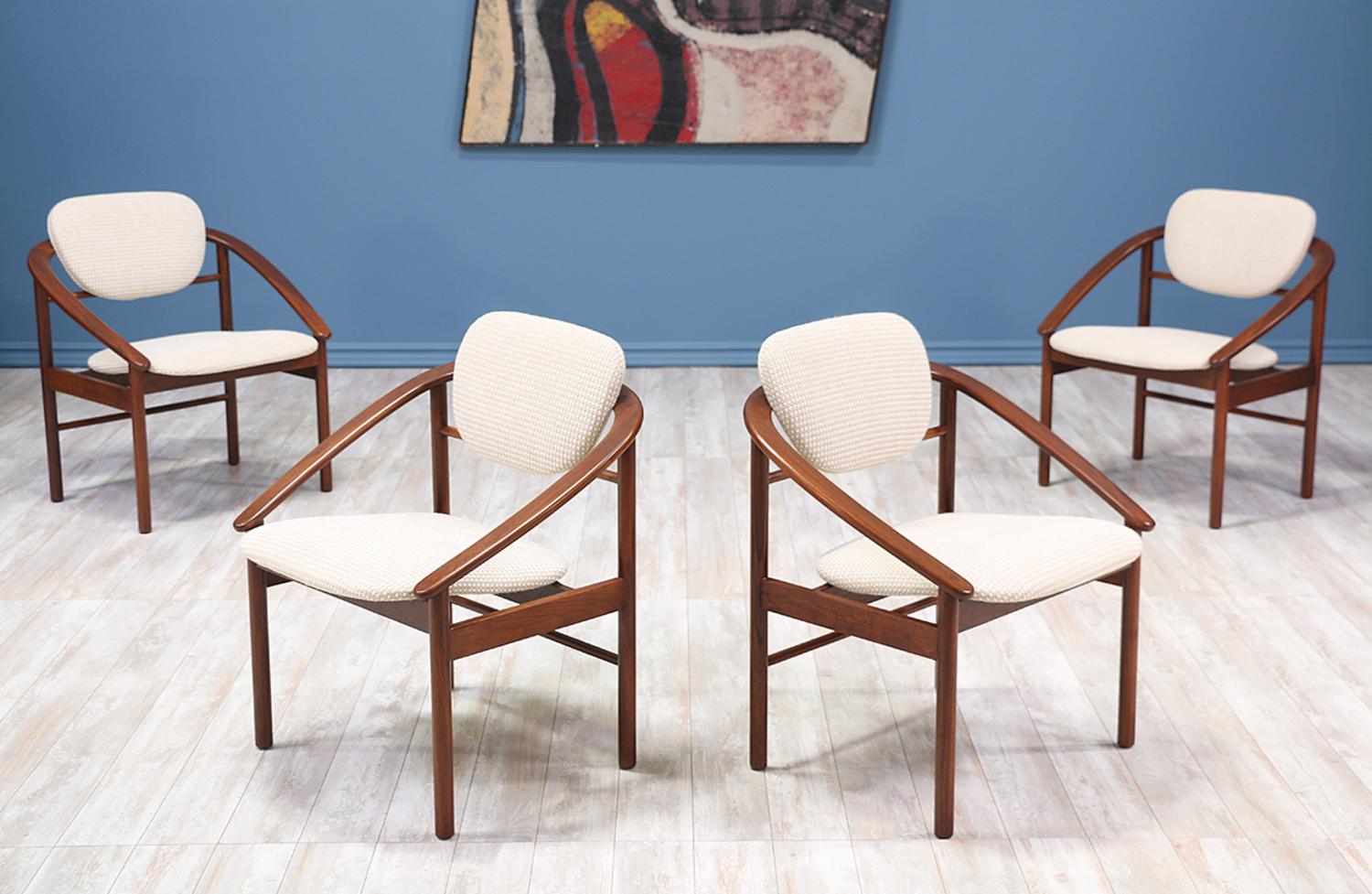 A set of four dining chairs designed by John Keal for Brown Saltman in the United States circa 1960s. This set features a rounded backrest connected to sloping arms that contrast beautifully with the linear frame. This unique set of dining chairs