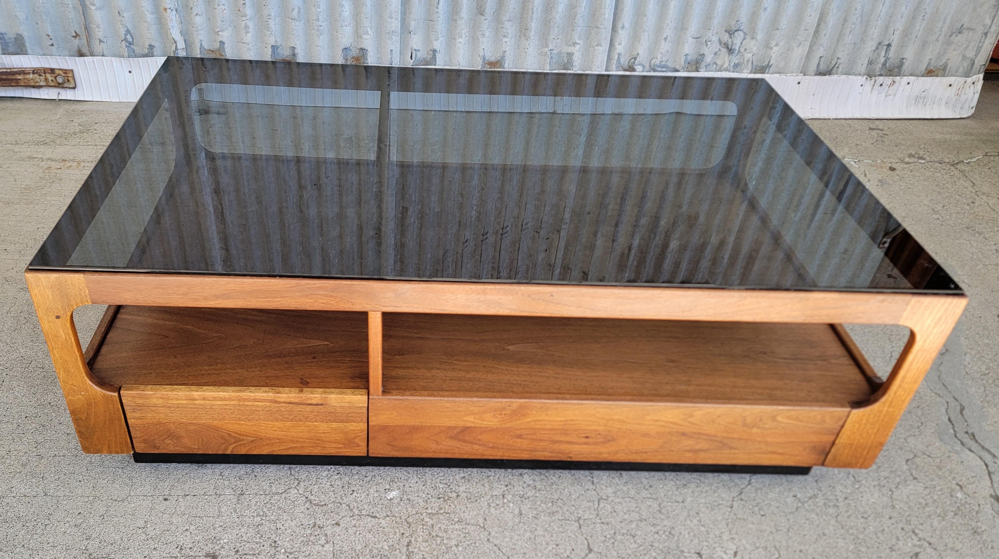 Mid-Century Modern rectangular coffee table designed by John Keal for brown Saltman of California. Circa. 1960.  Features storage or display under smoked glass top and two drawers at table base. Crafted in solid walnut. In very good original vintage