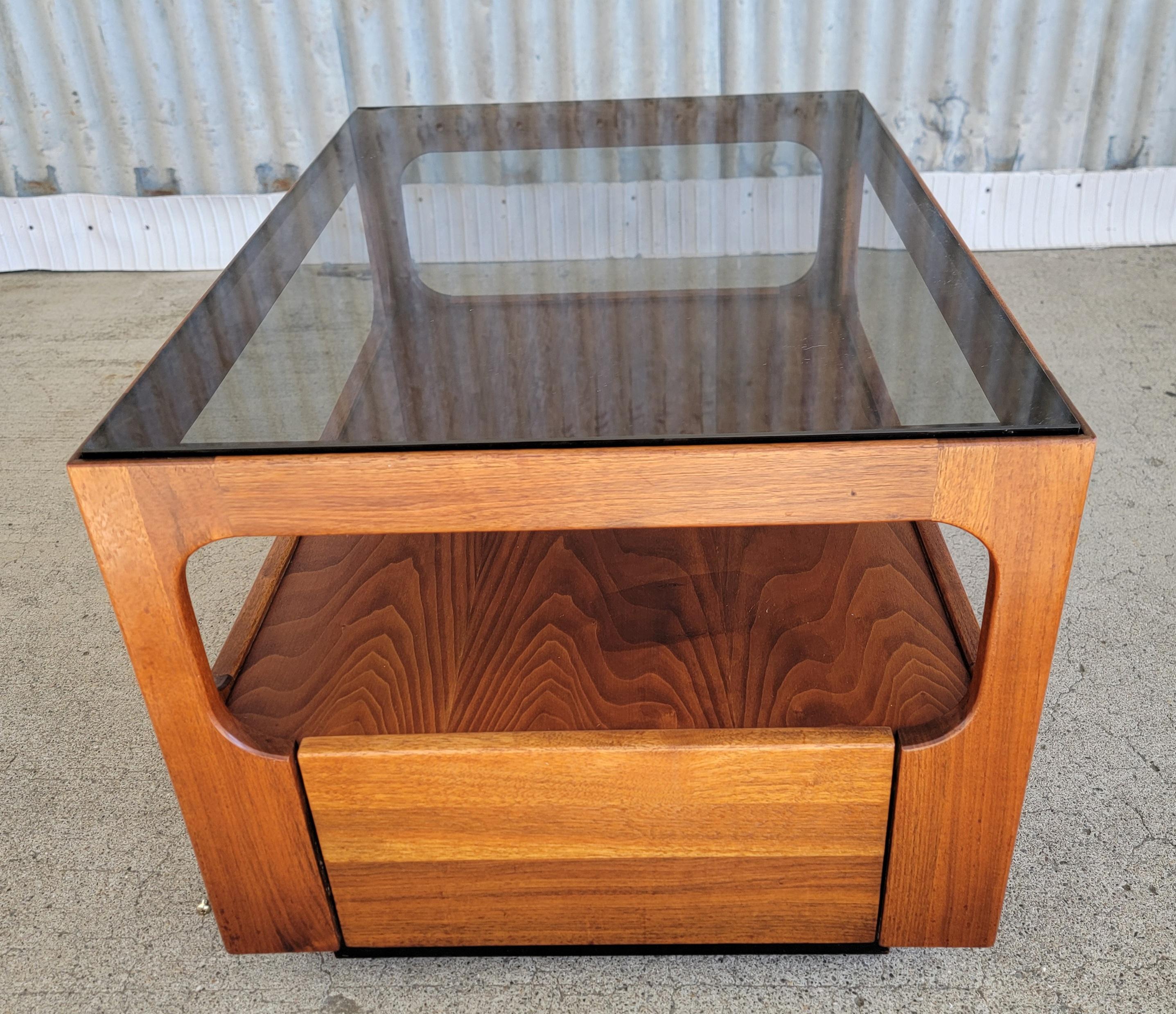 A Mid-Century Modern end or side table crafted in solid walnut with a smoked glass top. Designed by John Keal for Brown Saltman of California, circa. 1960's. Features storage or display under glass top and a single drawer at front of table. Retains