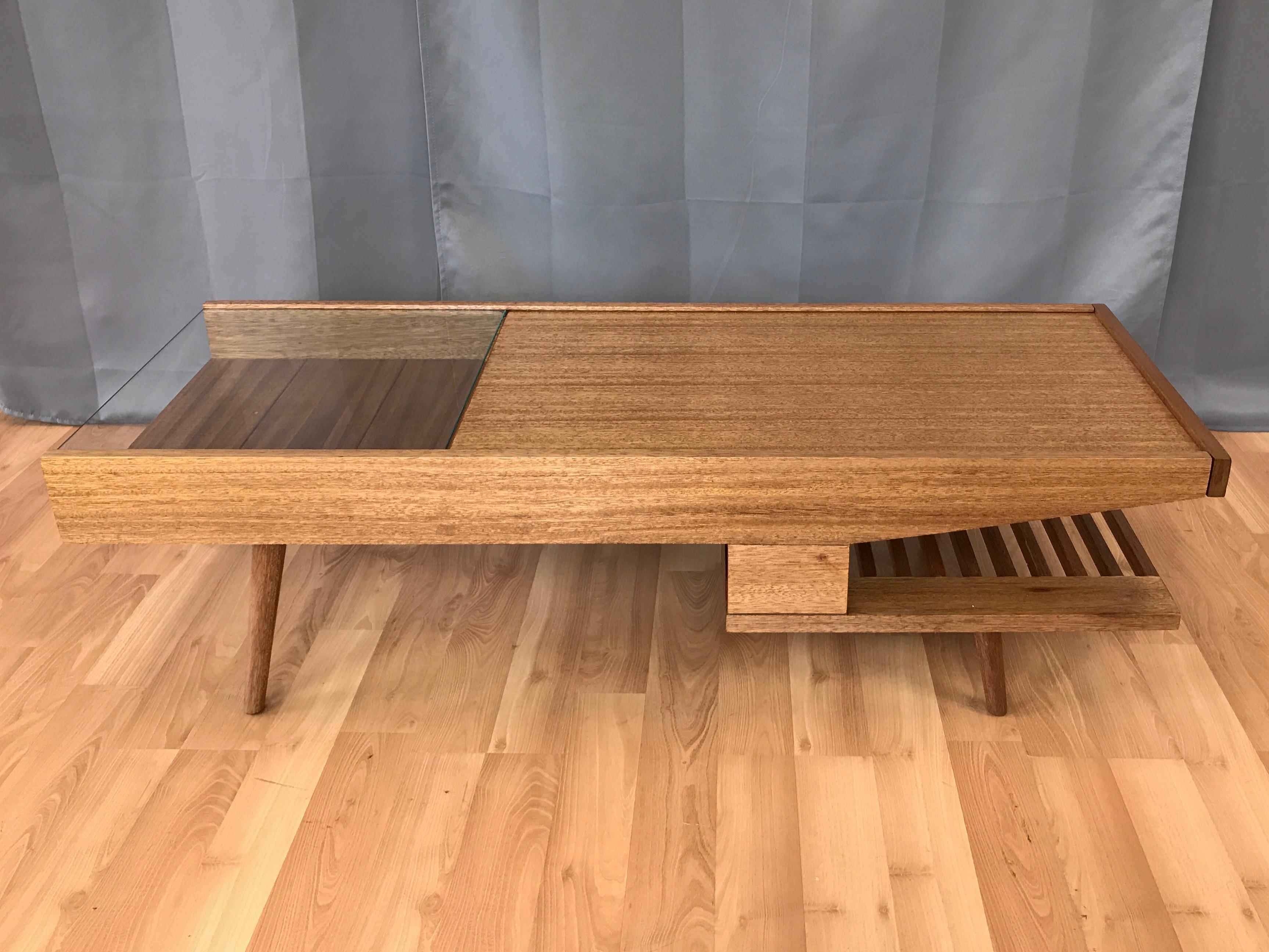 A fantastic and rare Mid-Century Modern mahogany and glass coffee table with concealed laminate serving surface and built-in warming plate by John Keal for Brown-Saltman.

Gorgeously grained golden ribbon mahogany with wood and glass top, open