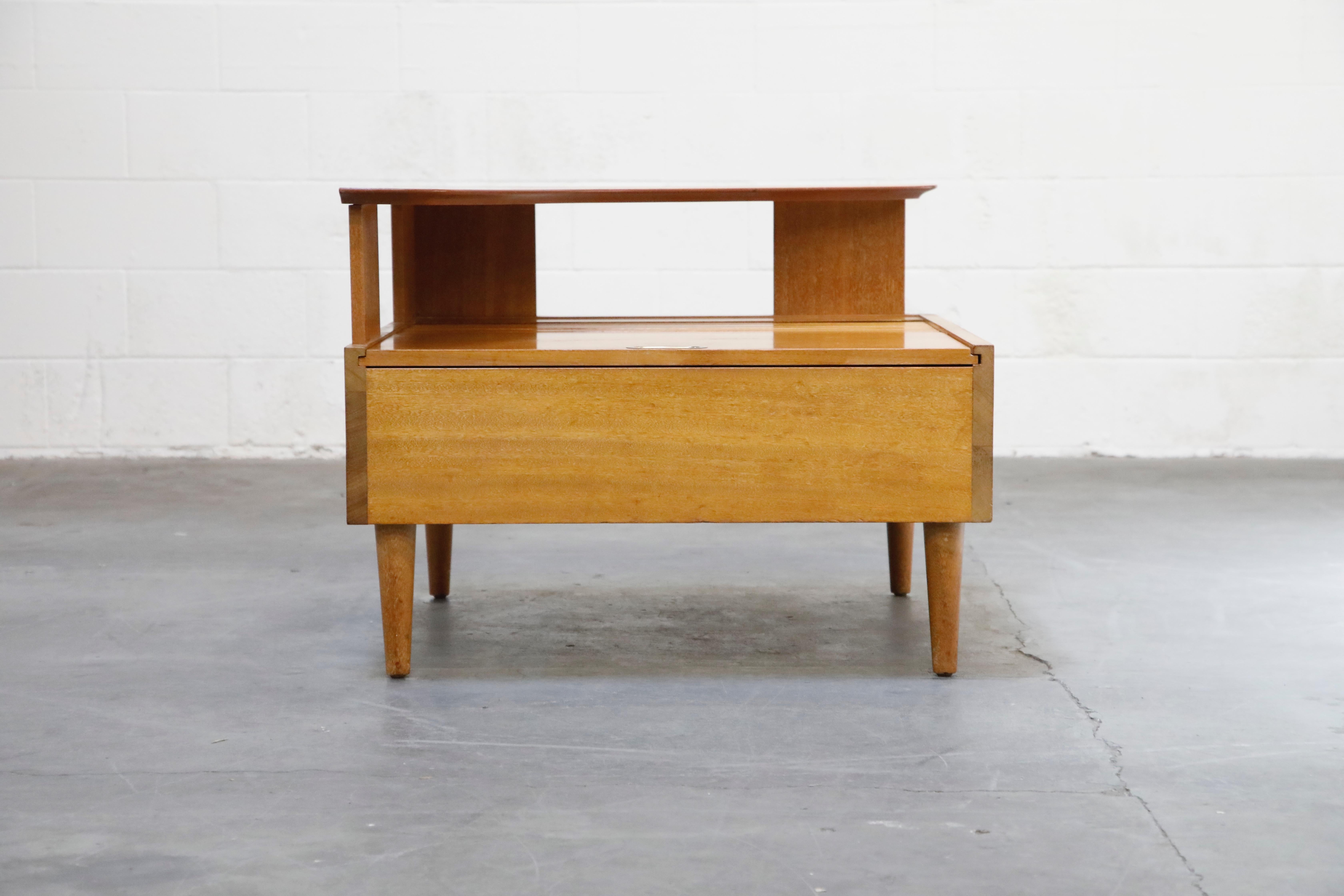This spacious John Keal for Brown-Saltman, circa 1960, tiered corner table features a boomerang upper shelf over a tambour pullback door which opens to a spacious storage area, raised on cylindrical tapering legs. The interior of this bleached