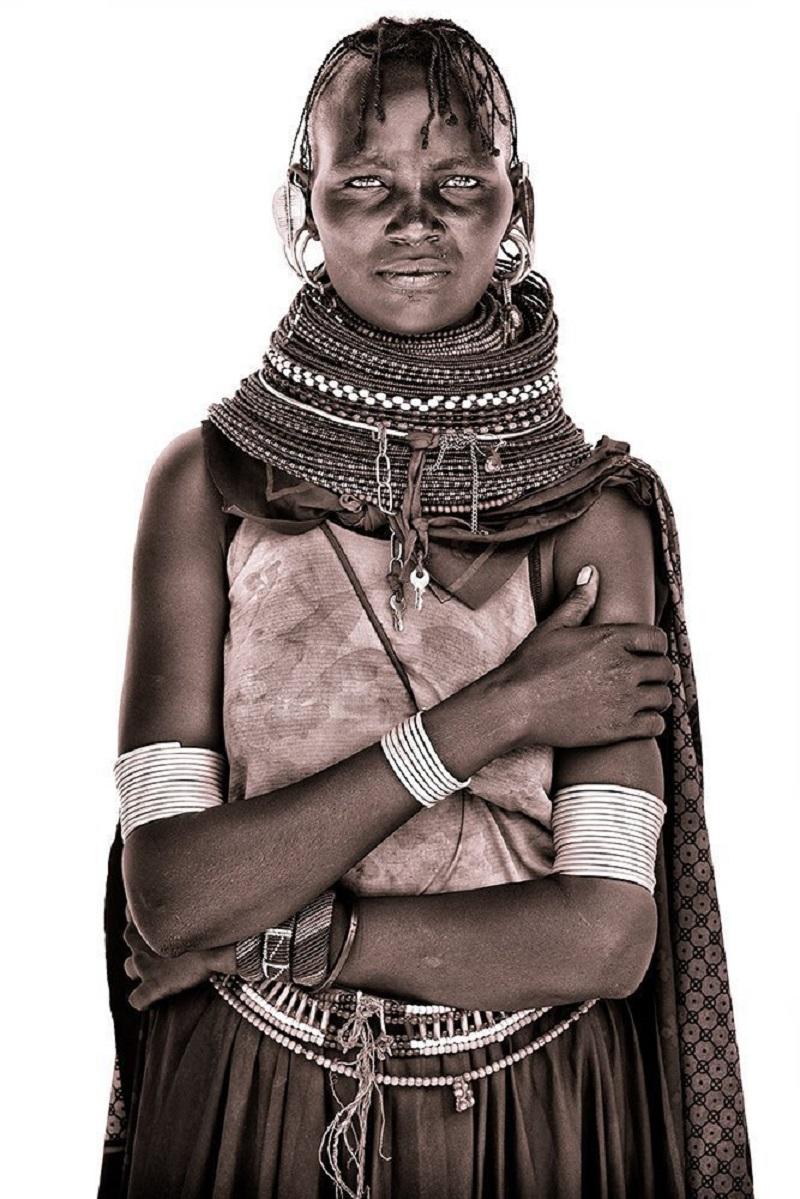 A portrait of a beautiful young Turkana woman photographed on the banks of Lake Turkana.

John uses simple natural light and builds primitive makeshift studios from locally acquired white sheets! The suffuse light allows him to capture a remarkable