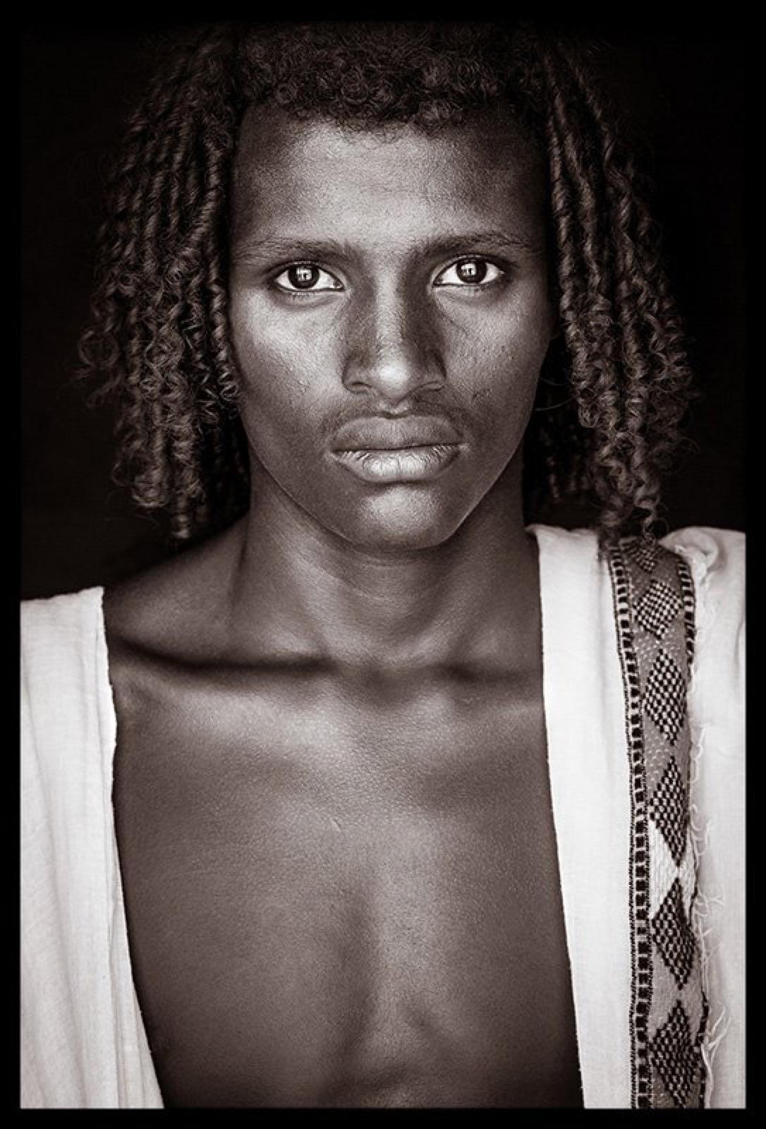 Ein junger Mann aus der Afar-Kultur in der Stadt Assaita.  Viele Männer verbringen die Nachmittage mit lauten Debatten in Lehmhäusern und Höfen.  Oft mit einer Handvoll Miraa-Blätter (ghat) und mit der Droge gefüllten Wangen. Dieses gesellige