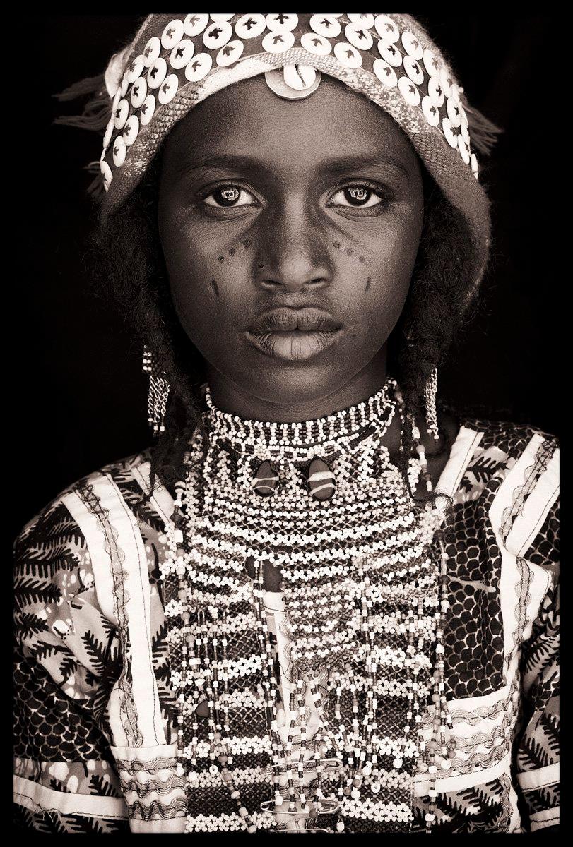 John met this young Fula girl as she was walking across the barren, sandy monotones of Niger’s Sahel. She was wearing an amazingly intricate arrangement of beads and a carefully crafted hat.

The intricate jewellery and vibrant facial make-up