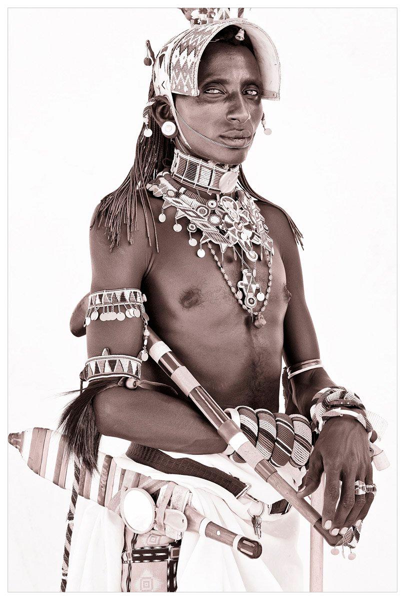 Wie viele der Samburu legt auch dieser Krieger großen Wert auf sein Äußeres. Abgesehen von der Menge an Schmuck, die er trägt, gibt es zwei Anzeichen, die ihn verraten: ein kleiner rosafarbener Taschenspiegel neben seinem Schwert und ein Beutel an