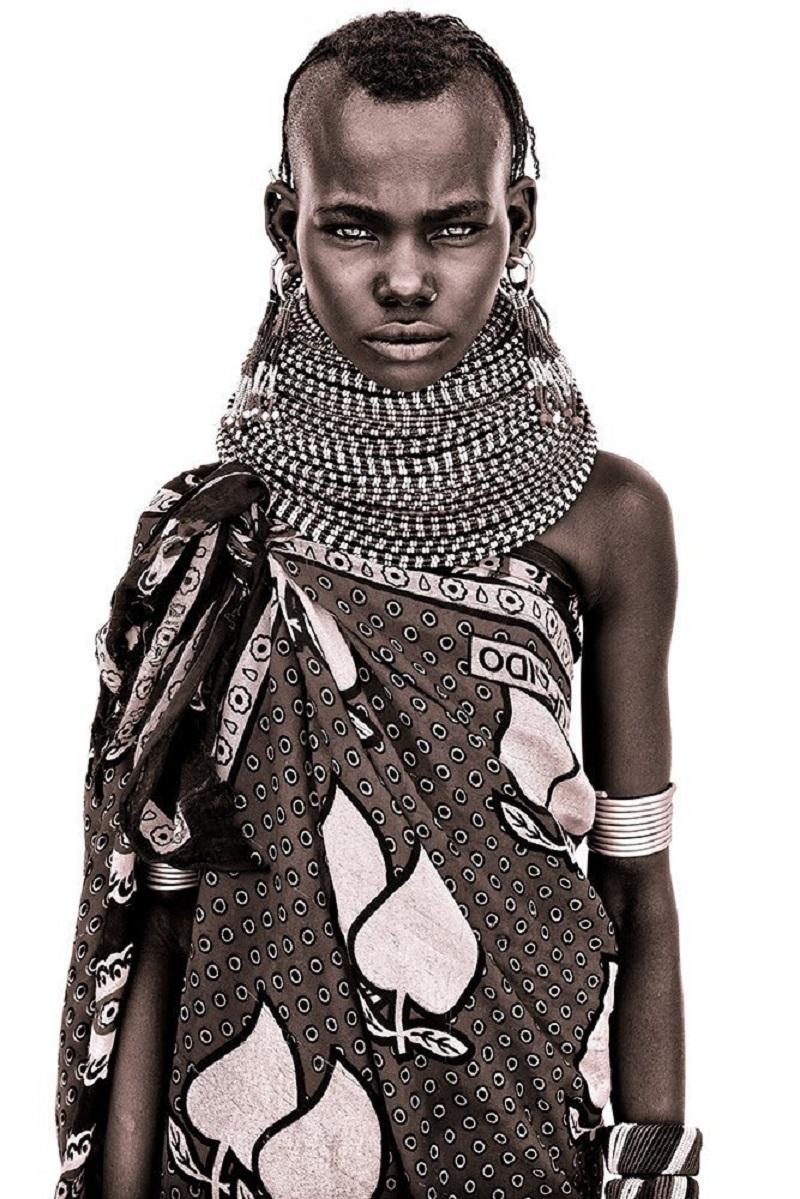 A young Turkana girl

John uses simple natural light and builds primitive makeshift studios from locally acquired white sheets! The suffuse light allows him to capture a remarkable level of detail. His subjects calm demeanor belies the reality of