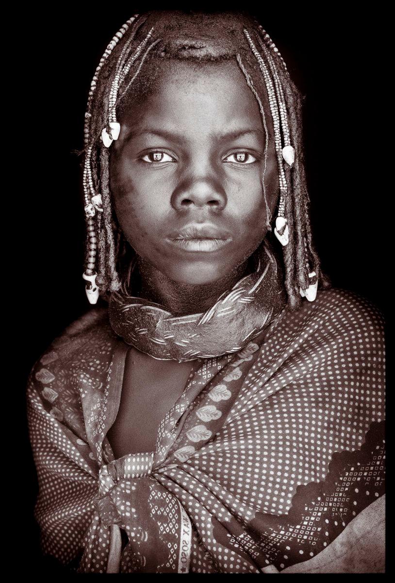 Nambuele veranschaulicht die Haarkunst der Mumuhuila im Süden Angolas, deren Frauen wie besessen auf ihre Frisur achten.  Auch wenn sie sich im Laufe der verschiedenen Lebensabschnitte eines Mädchens ändern können, ergänzen sie immer den natürlichen