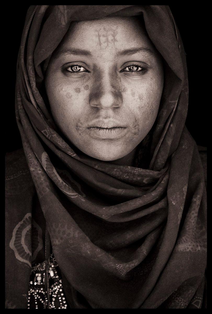 John met this Wodaabe girl who was carrying her young child in a remote market village called Sakabal in the far north of Niger’s Maradi province. Like many Wodaabe women, she had many permanent tattoos on her face; you can clearly see the tattoos