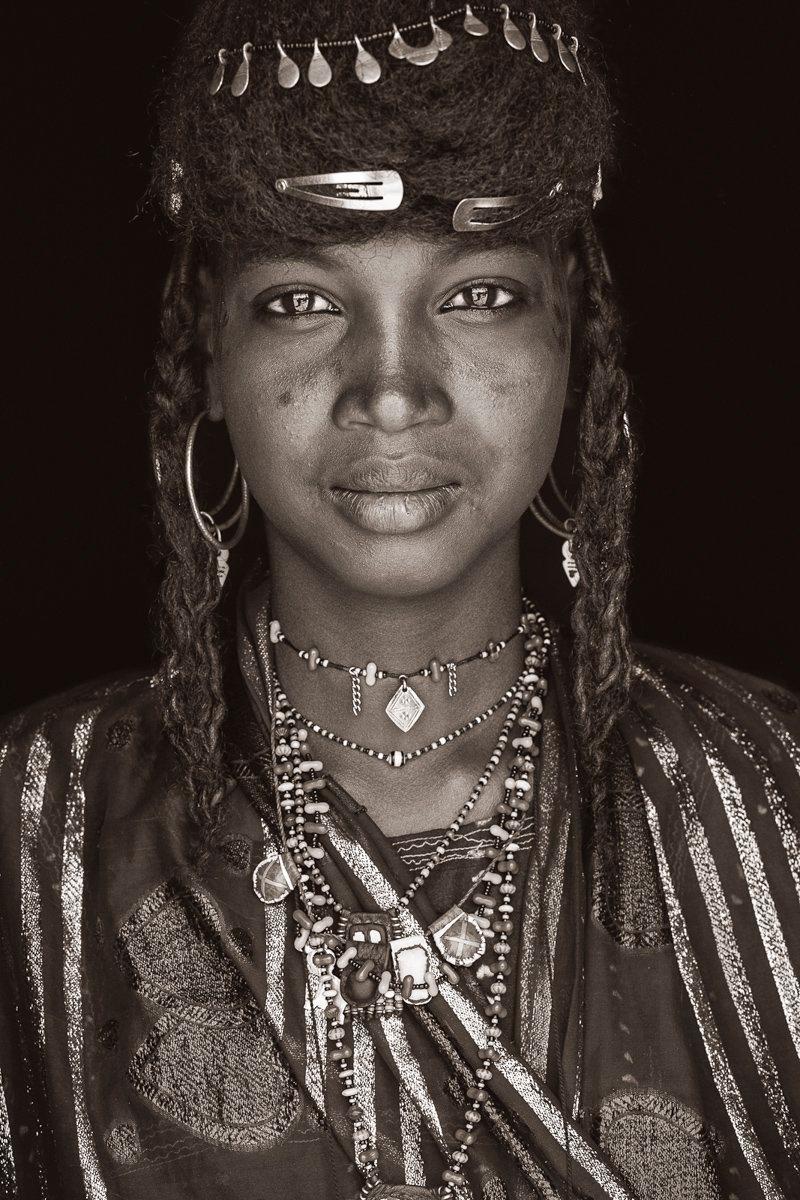 A young Wodaabe maiden from Niger.

John Kenny’s work is all shot on location in some of the remotest corners of Africa. His images are all taken with natural light and his subjects in their day to day attire.

The C-type prints are mounted with an