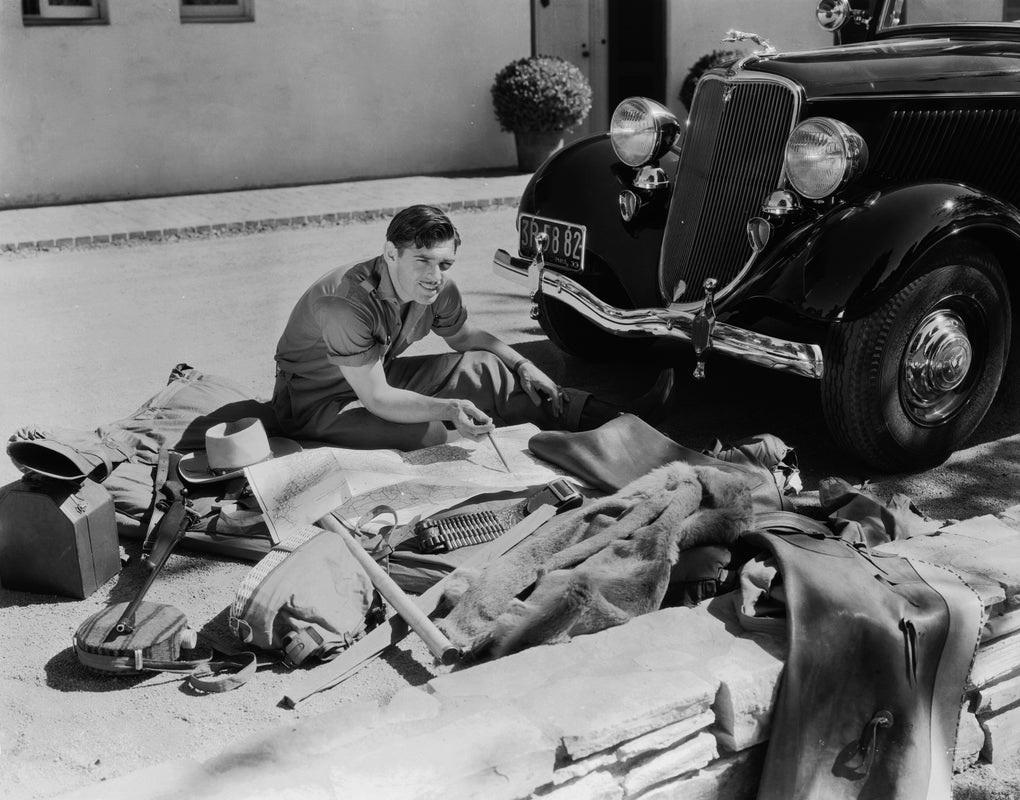 "Clarks große Flucht" von der John Kobal Foundation

17. Oktober 1933: Der amerikanische Schauspieler Clark Gable (1901 - 1960) sitzt vor seinem Auto und plant seine Reise mit einer Landkarte vor sich und seinen Reiseutensilien, die um ihn herum