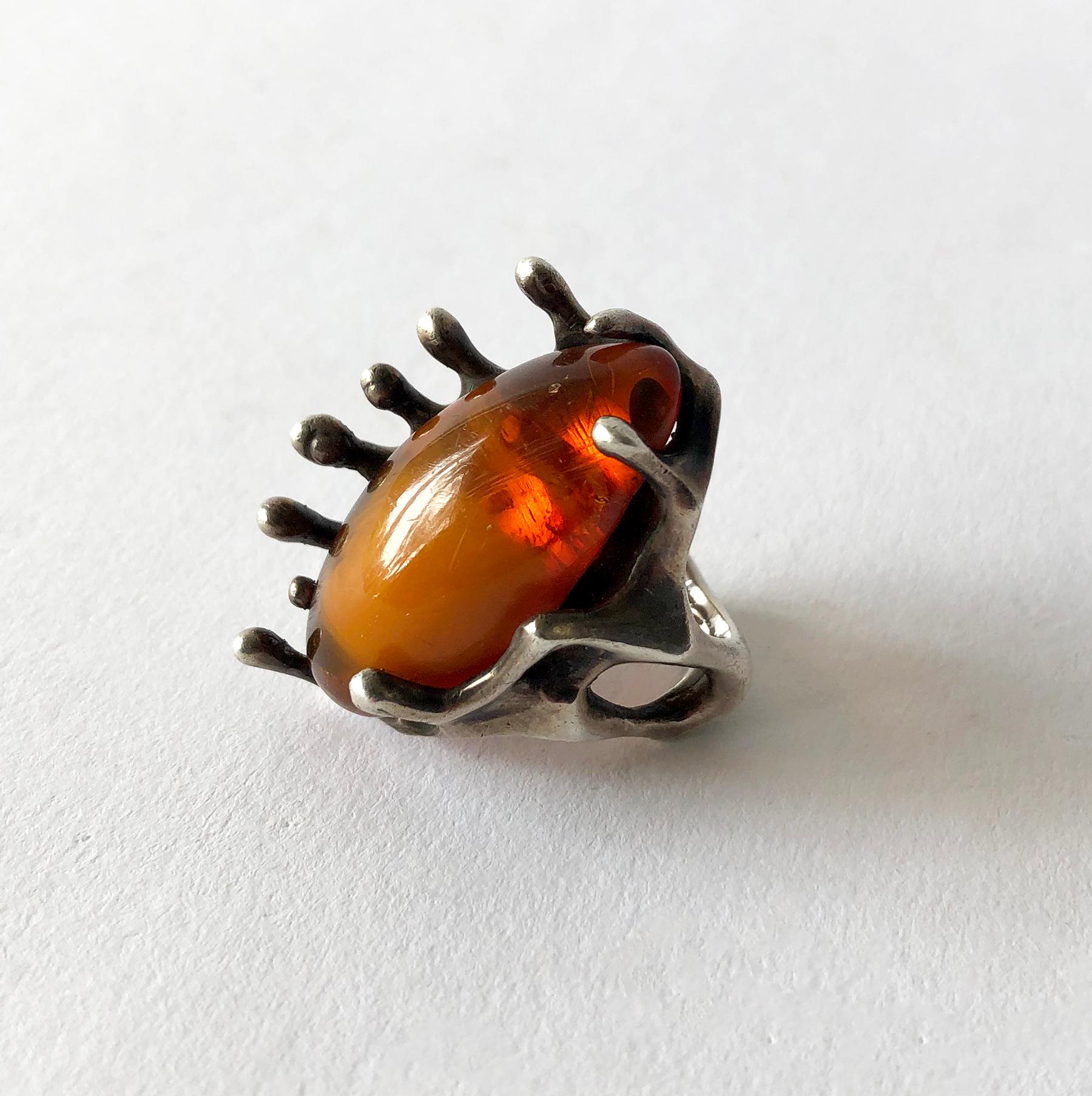 Large oval amber cabochon set in a brutalist setting of sterling silver made by John M. Morgan of Ellensburg, Washington. Ring is a finger size 7.5 - 8 due to its unusual design. The face of the ring measures about 1.5