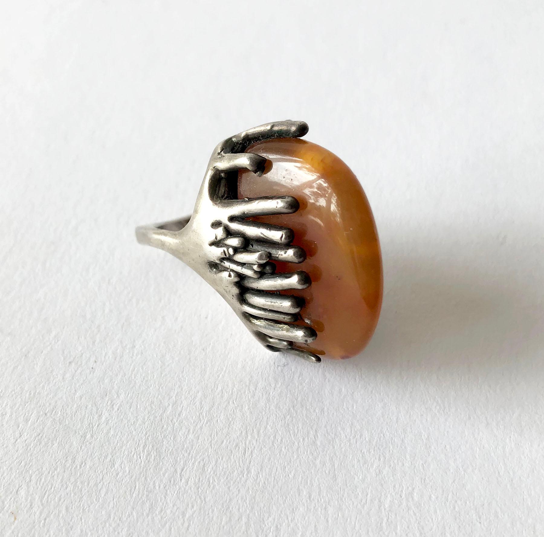 Gorgeous piece of amber in pebble form, set in a brutalist setting of sterling silver made by John M. Morgan of Ellensburg, Washington. Ring is a finger size 6.25 - 6.5 due to its unusual design. The face of the ring measures about 1 1/8
