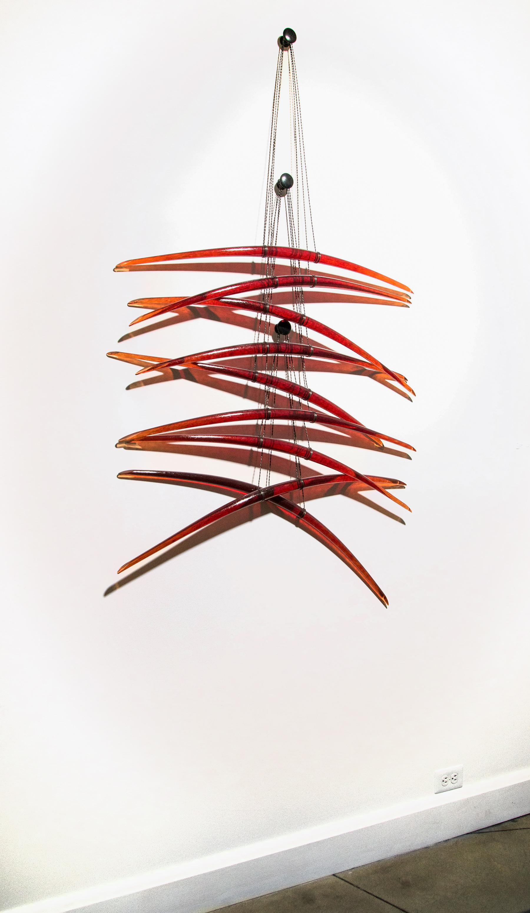 Elegantly curved deep red glass pieces in twos are suspended on fine black steel cables in this dramatic new wall sculpture by Canadian artist John Paul Robinson. His glass work is inspired by nature’s elements—earth, wind, fire and water. The