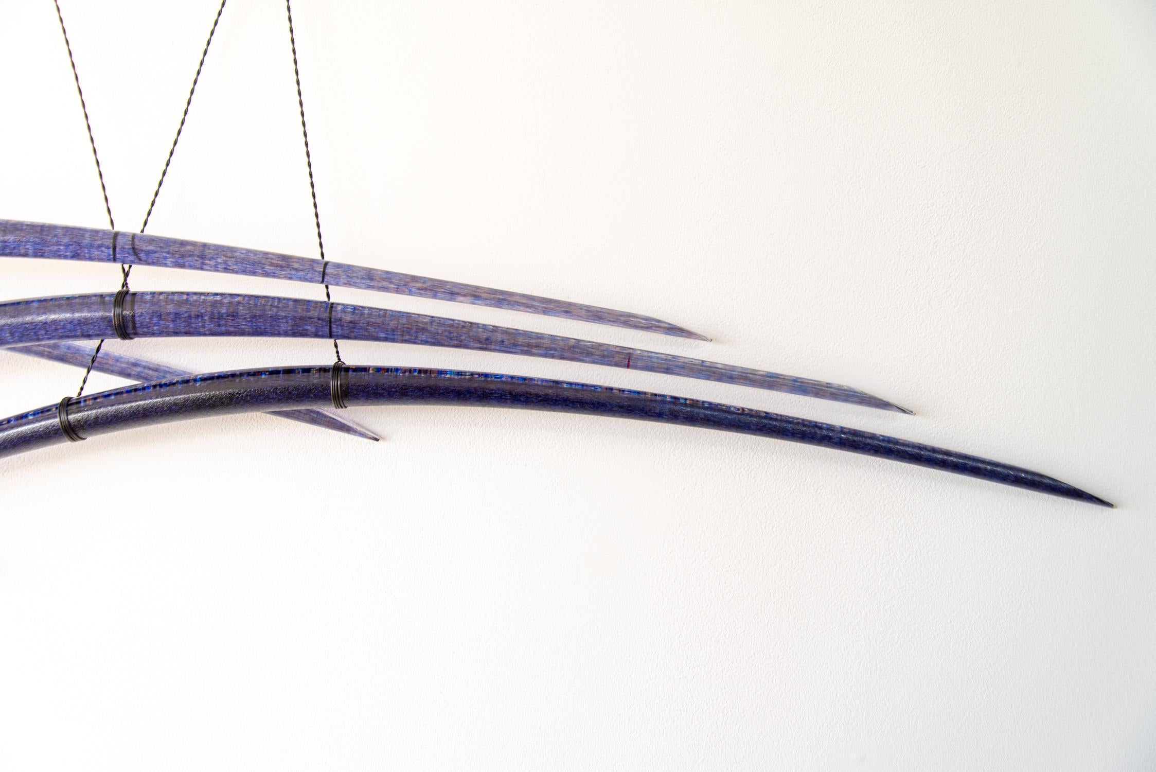 Canadian artist John Paul Robinson has chosen a deep blue for this elegant glass wall sculpture. Six arched pieces of translucent glass are suspended by fine steel cables…each crisscrossing the other in a graceful composition.
His glass work is