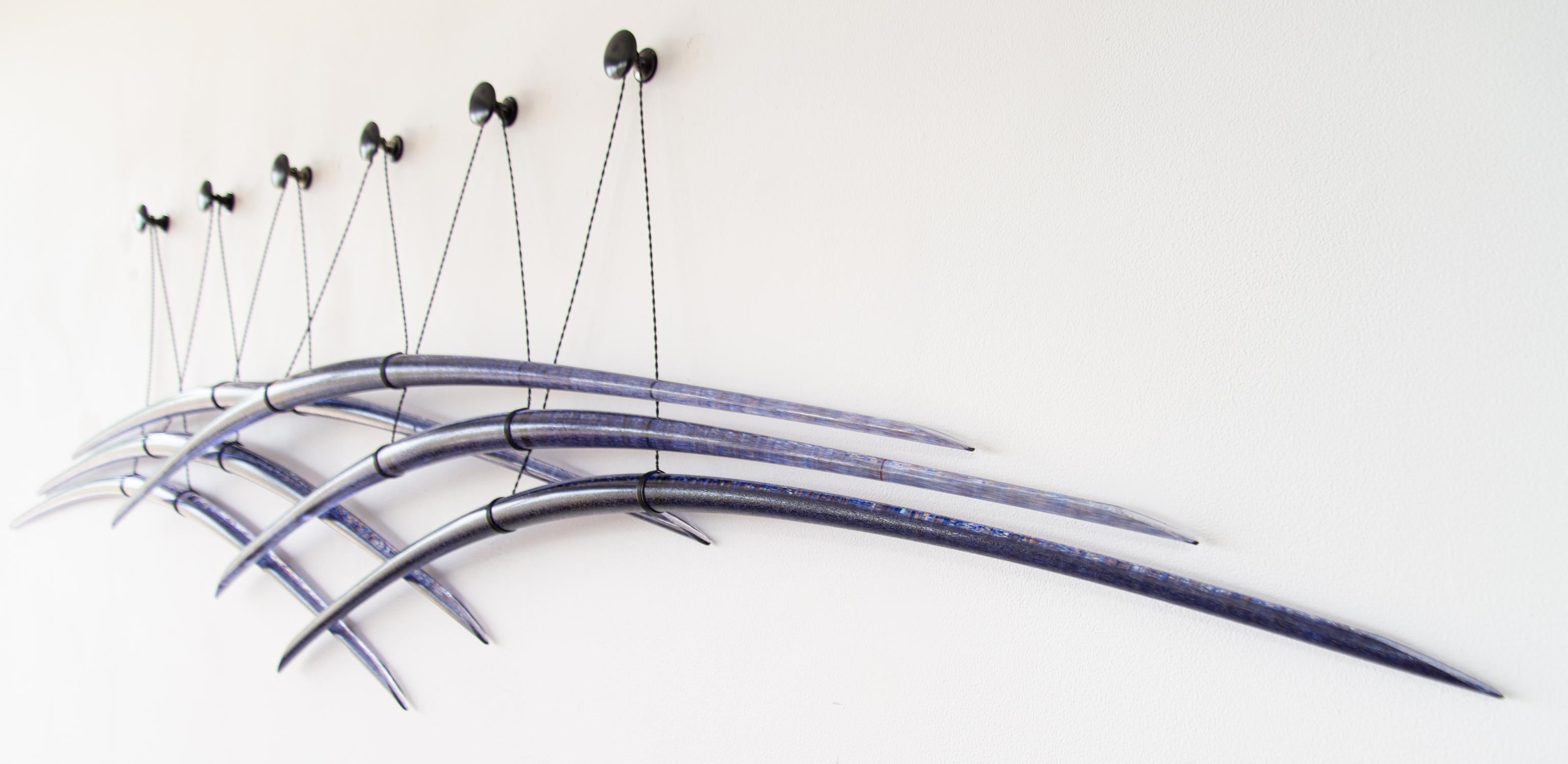 Canadian artist John Paul Robinson has chosen a deep blue for this elegant glass wall sculpture. Six arched pieces of translucent glass are suspended by fine steel cables…each crisscrossing the other in a graceful composition.
His glass work is