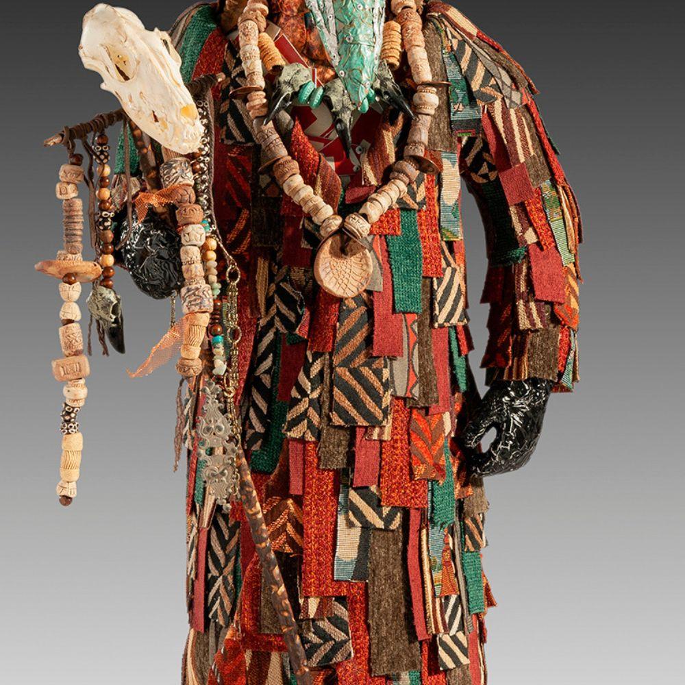 John Petrey’s Shaman is a striking mixed-media sculpture that merges mythology, ritual, and contemporary artistry. The figure wears a robe of richly patterned patchwork, assembled from reclaimed materials, creating a vibrant interplay of color and