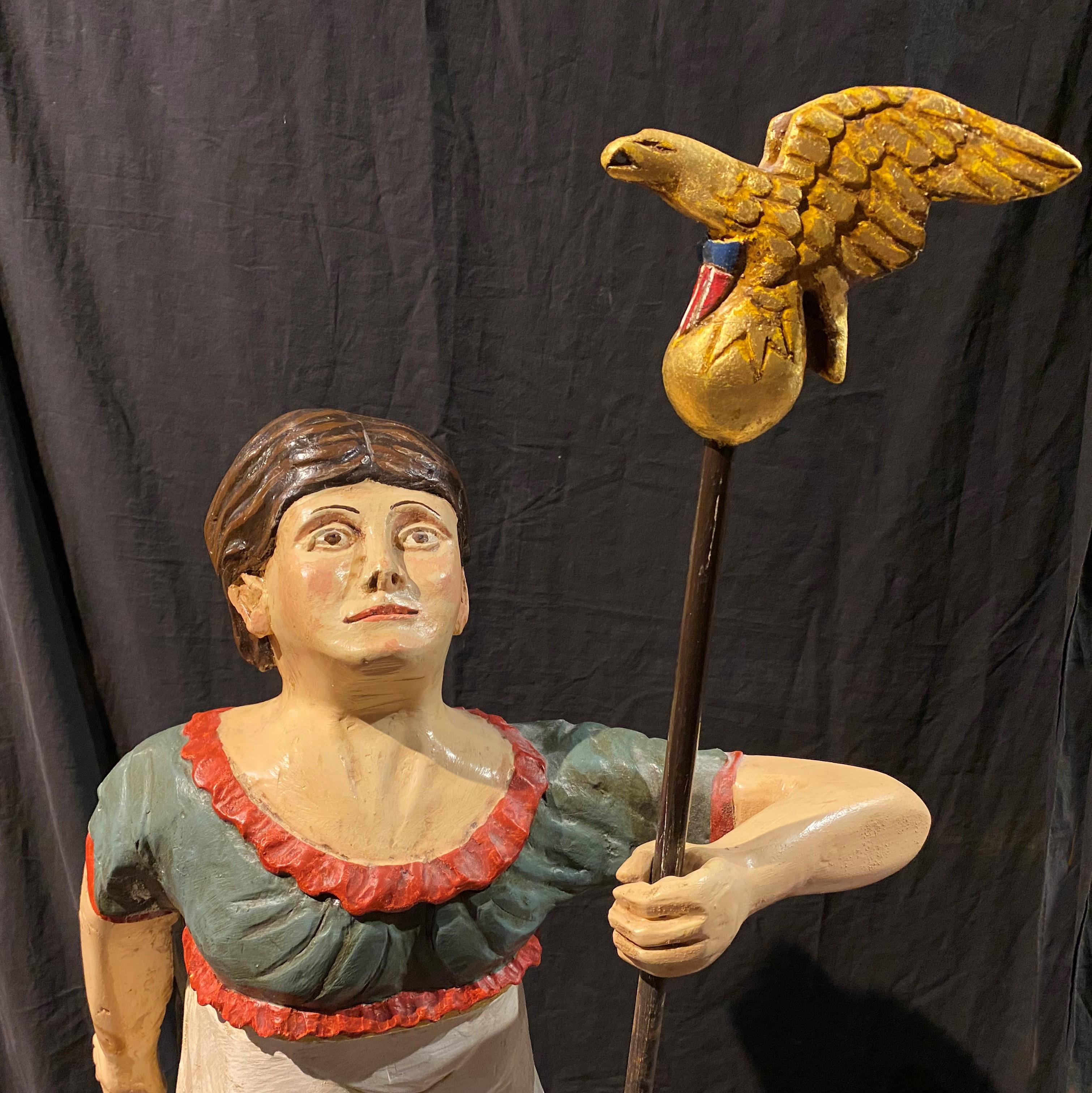 A fine 20th century American School hand carved folk art polychrome ship’s Lady Liberty figurehead on a separate wooden plinth, unsigned. The carved eagle baton is separate and fits into her hand. Acquired with several other carved figures with full