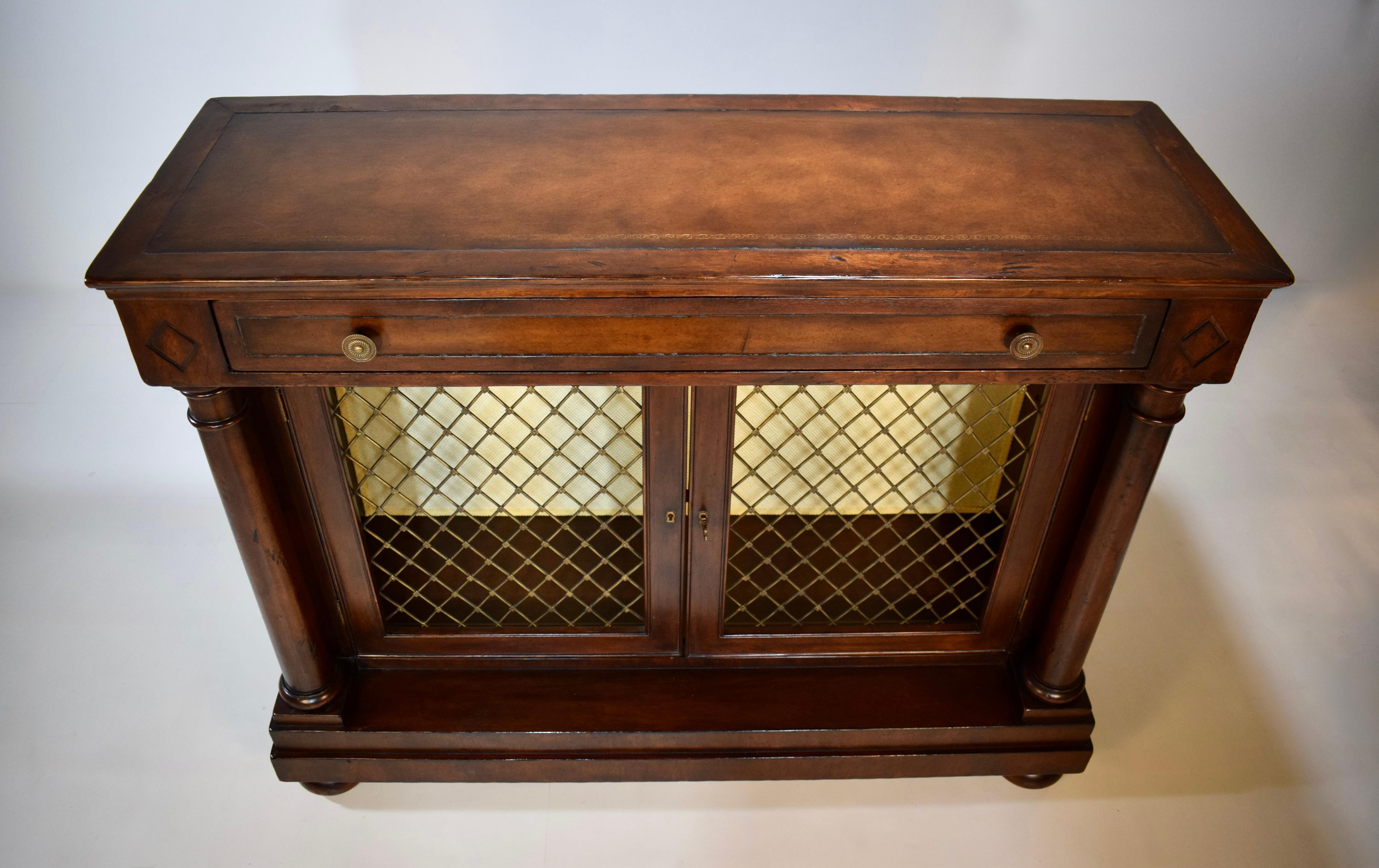Un imponente mobile libreria in stile Regency inglese con piano in pelle con lavorazione dorata e un unico cassetto. Due porte d'ingresso a traliccio in ottone traforato si ergono tra colonne toscane su una base a gradini su piedini a baldacchino.