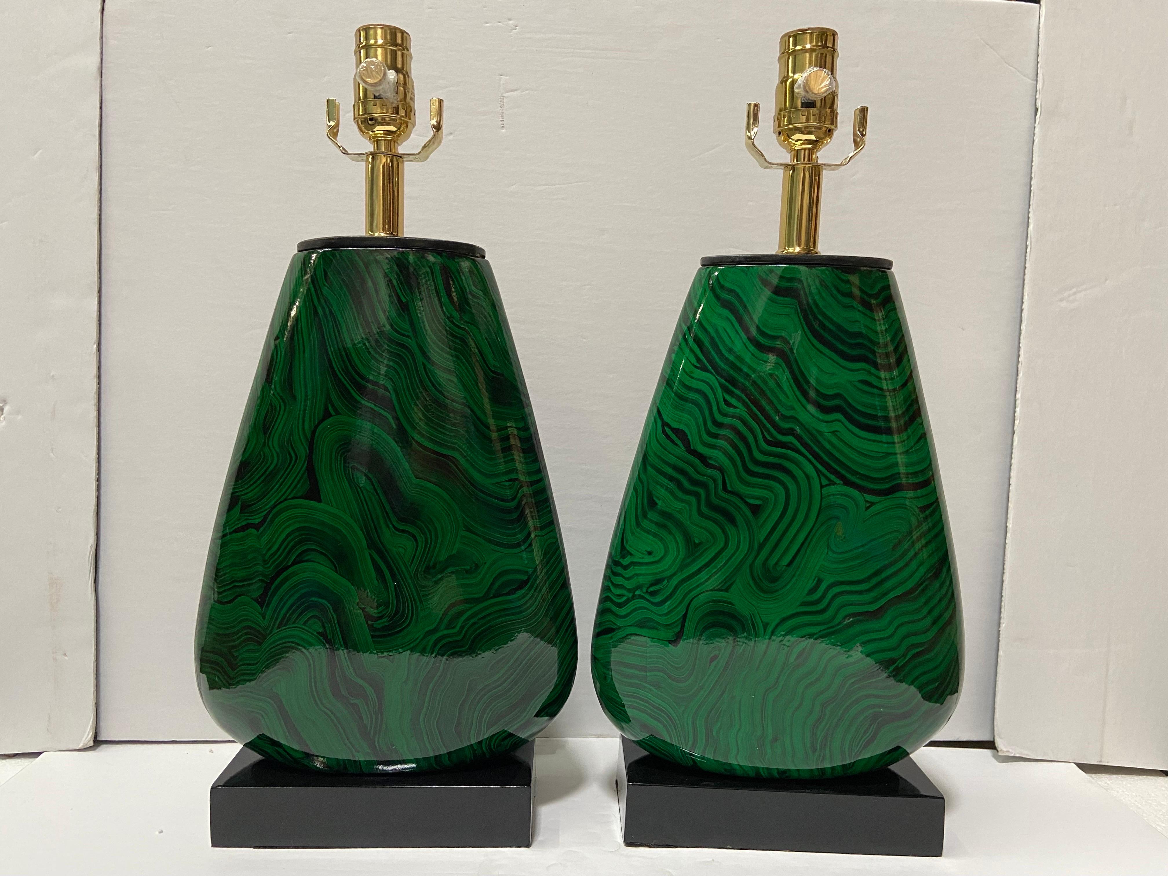 A vintage pair of faux malachite wood vessel forms by the John-Richard brand converted into table lamps. This pair of lamps features a wood vessel faux painted as malachite, set atop a rectangular black painted wood base. There is a black painted