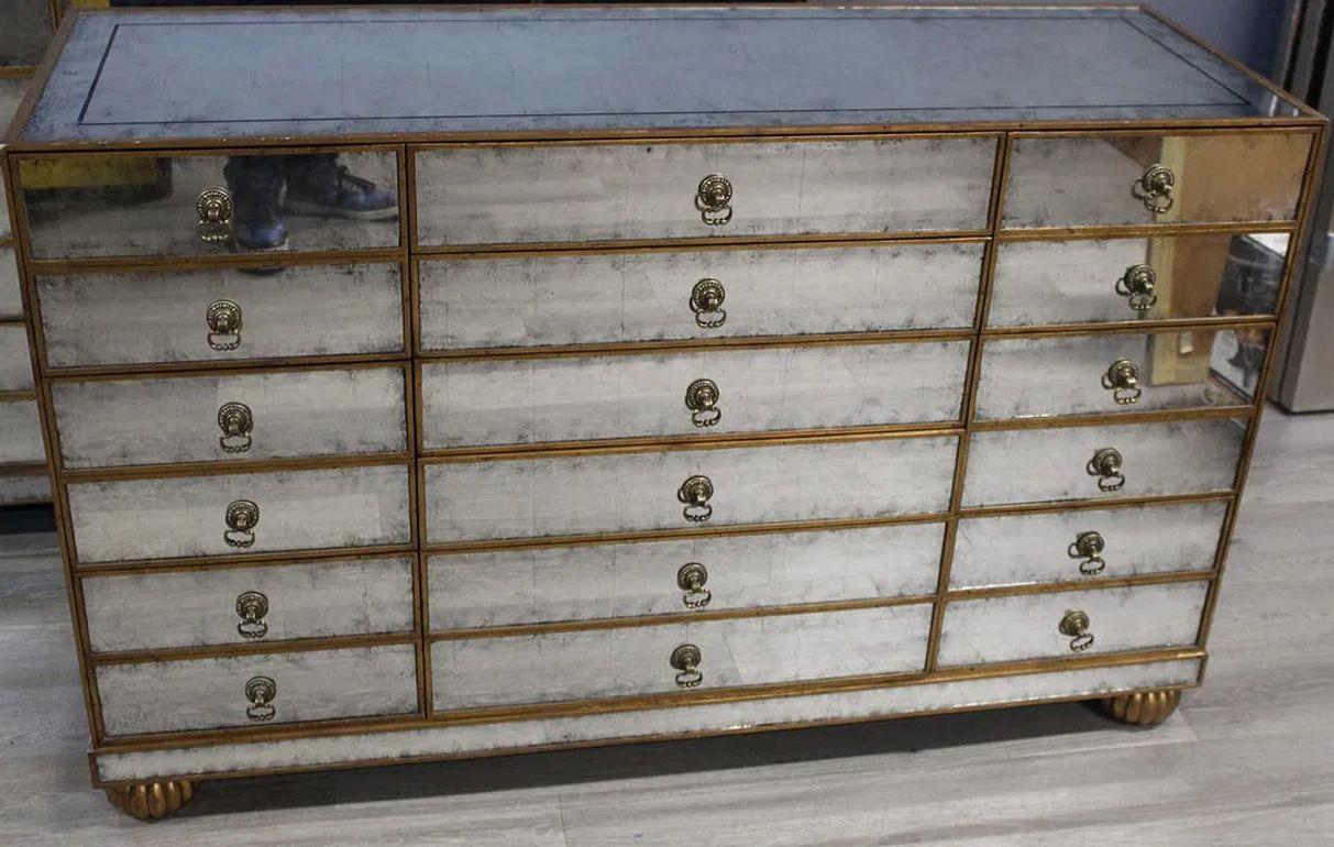 This elegant mirrored chest is a stunning piece that combines classic design with modern glamor. Featuring a distressed, antique finish on all mirrored surfaces, it has a rich, timeworn patina that adds character and depth. The gold-toned trim and